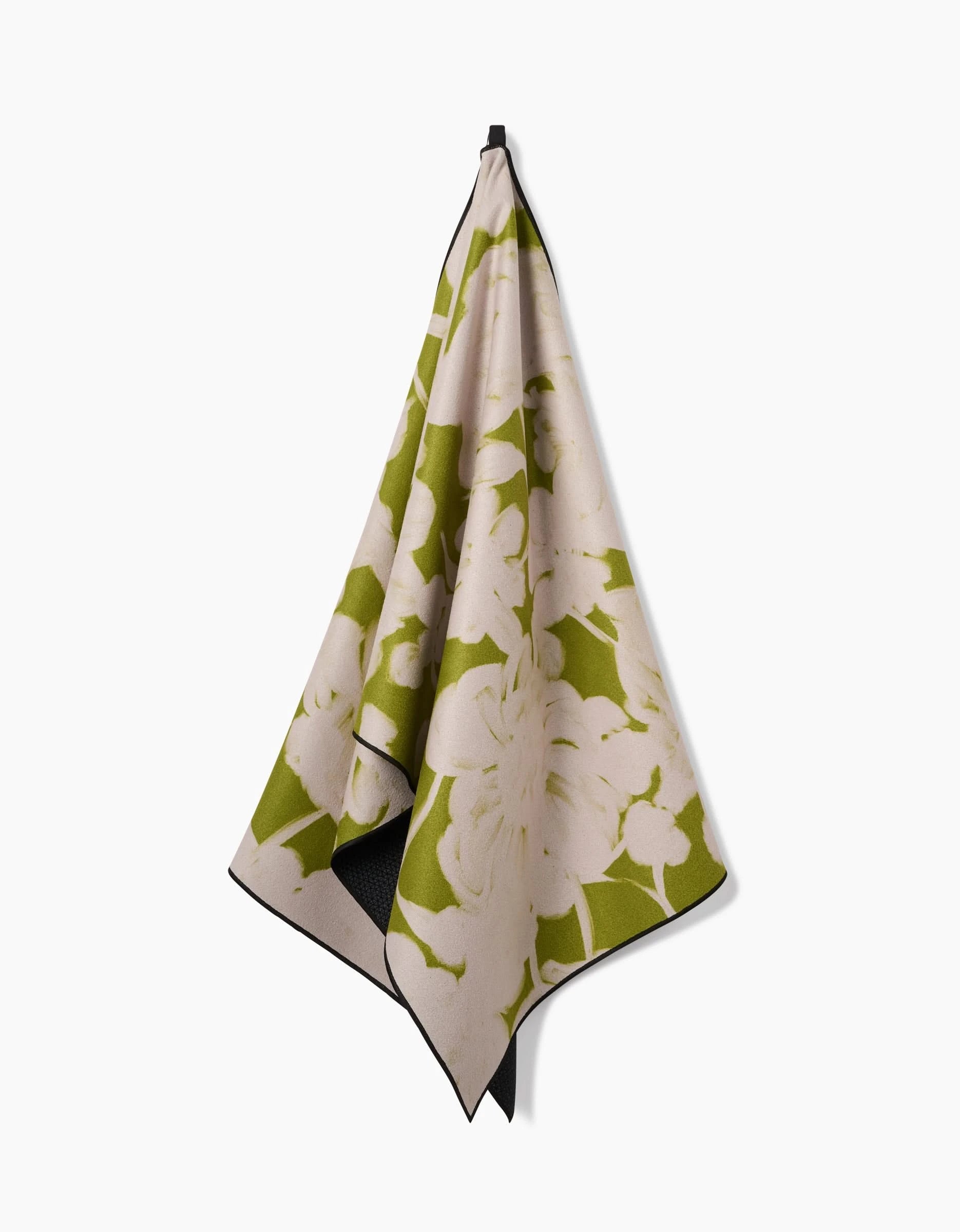 The GEOMETRY Meadow Mist yoga towel, crafted from recycled materials and featuring a green and beige floral pattern, hangs from a hook against a plain white background.