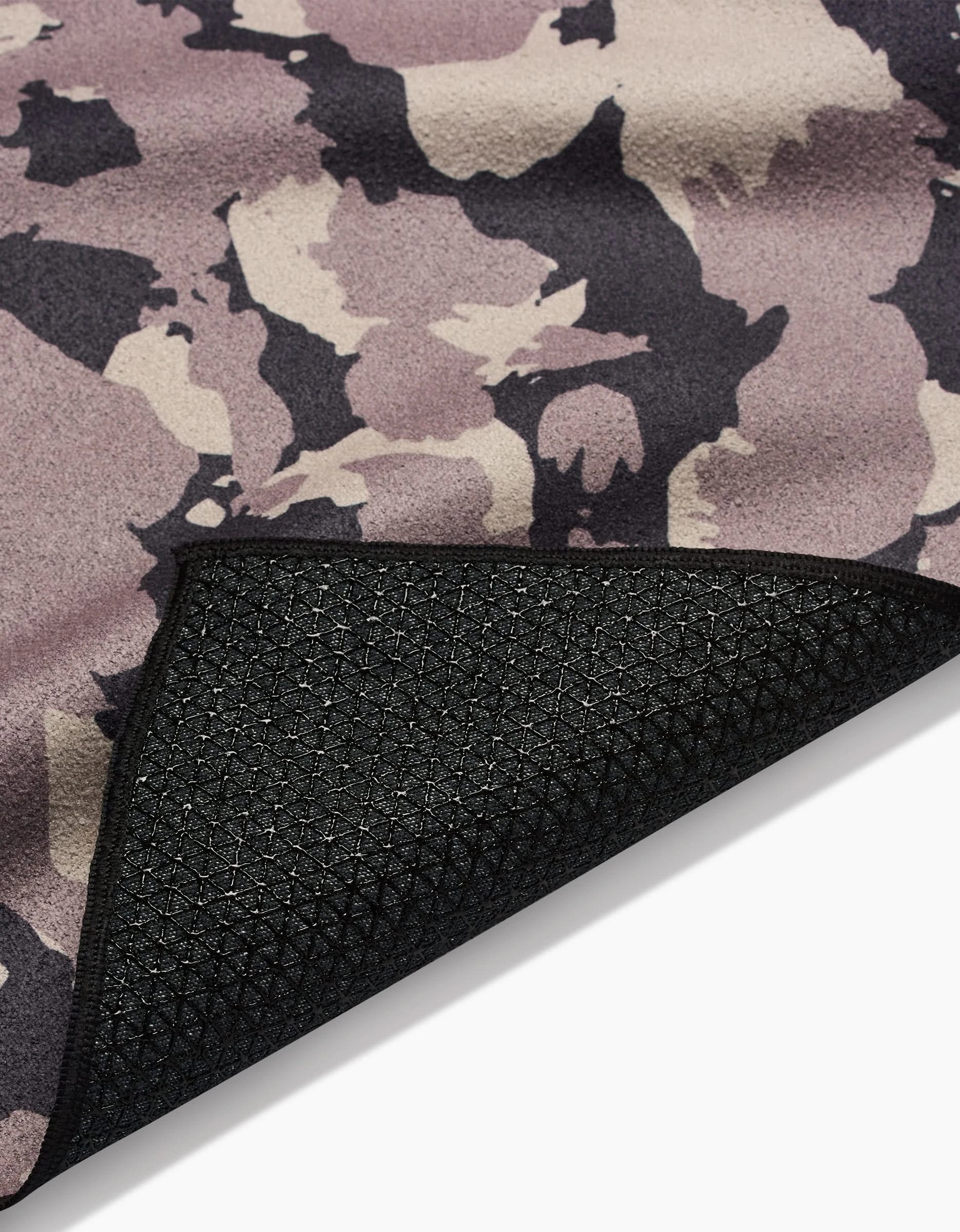 A close-up of the GEOMETRY Metro Mesh yoga towel in a purple, beige, and black camo pattern, featuring a flipped corner that reveals its textured black underside with geometric silicone grips for enhanced stability.