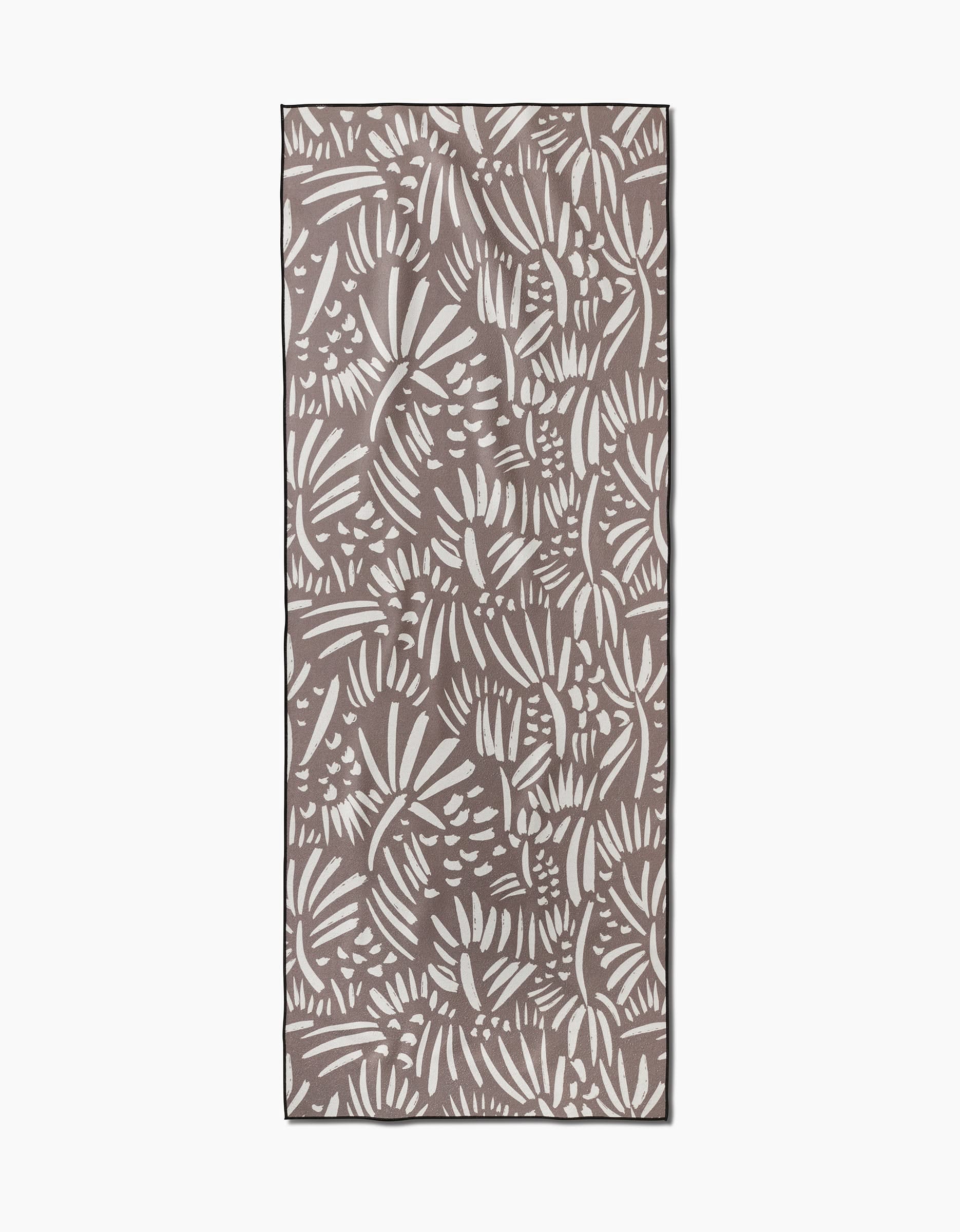 The Miami yoga towel by Hufton Studio is rectangular, made from recycled materials, and features a brown background with a white abstract leaf and botanical pattern across the entire surface.