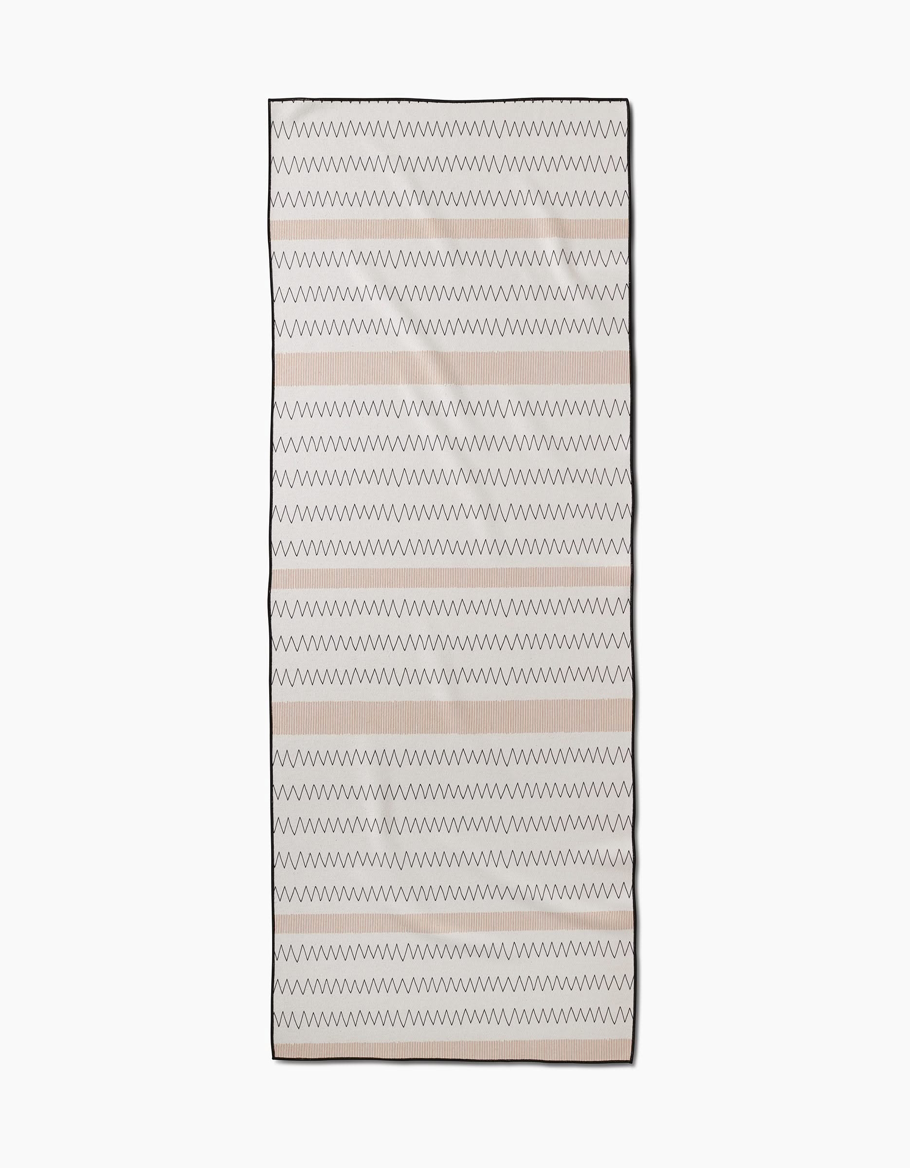 The Mod Zig Zag by Coit Creative is a rectangular beige recycled yoga towel featuring thin, evenly spaced horizontal black and light pink zigzag lines, shown against a white background.