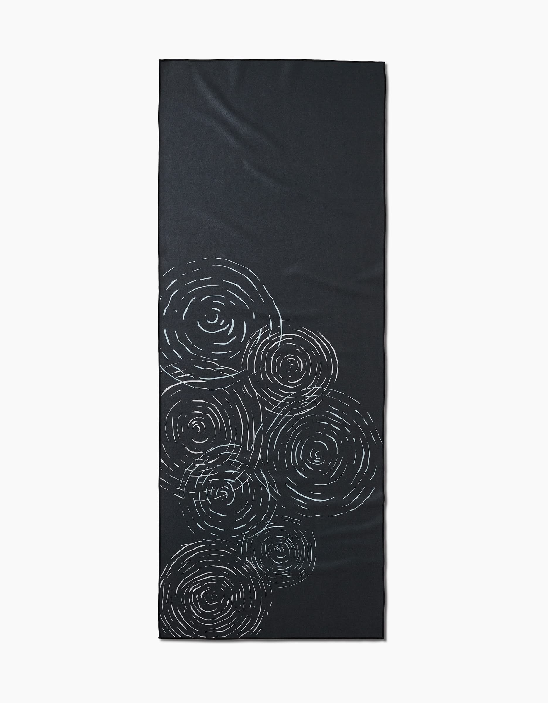 The GEOMETRY Om is a rectangular black yoga mat made from recycled materials, featuring white swirling circular patterns clustered on one end.