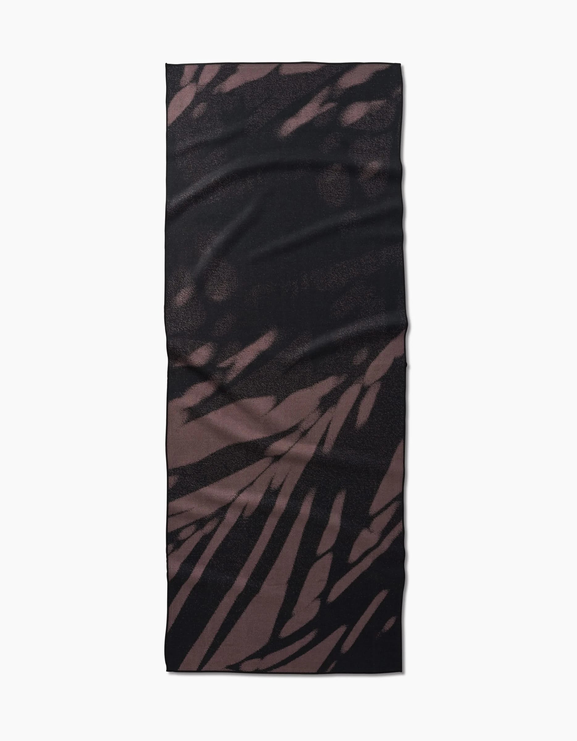 The GEOMETRY Palm Shadow is a rectangular yoga towel crafted from recycled materials, featuring an abstract streaked pattern in dark brown and black, displayed flat on a white background.