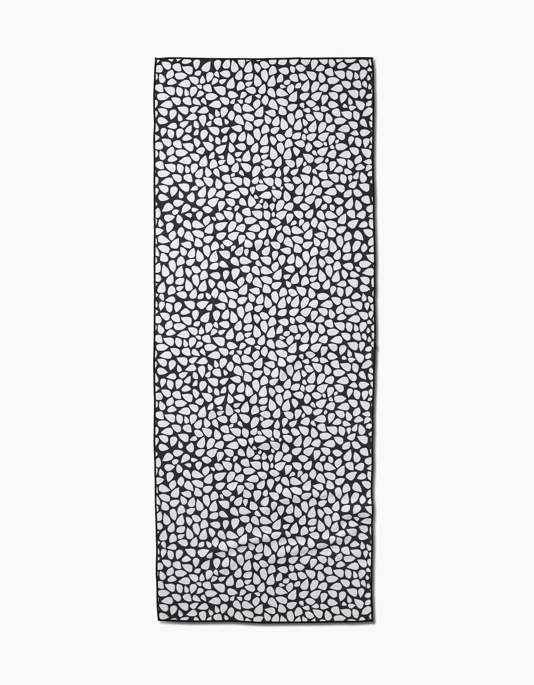 The Pebbles scarf by Marina Solodka features an all-over black pebble pattern on a white background, inspired by recycled yoga towels. The rectangular scarf is shown laid flat.