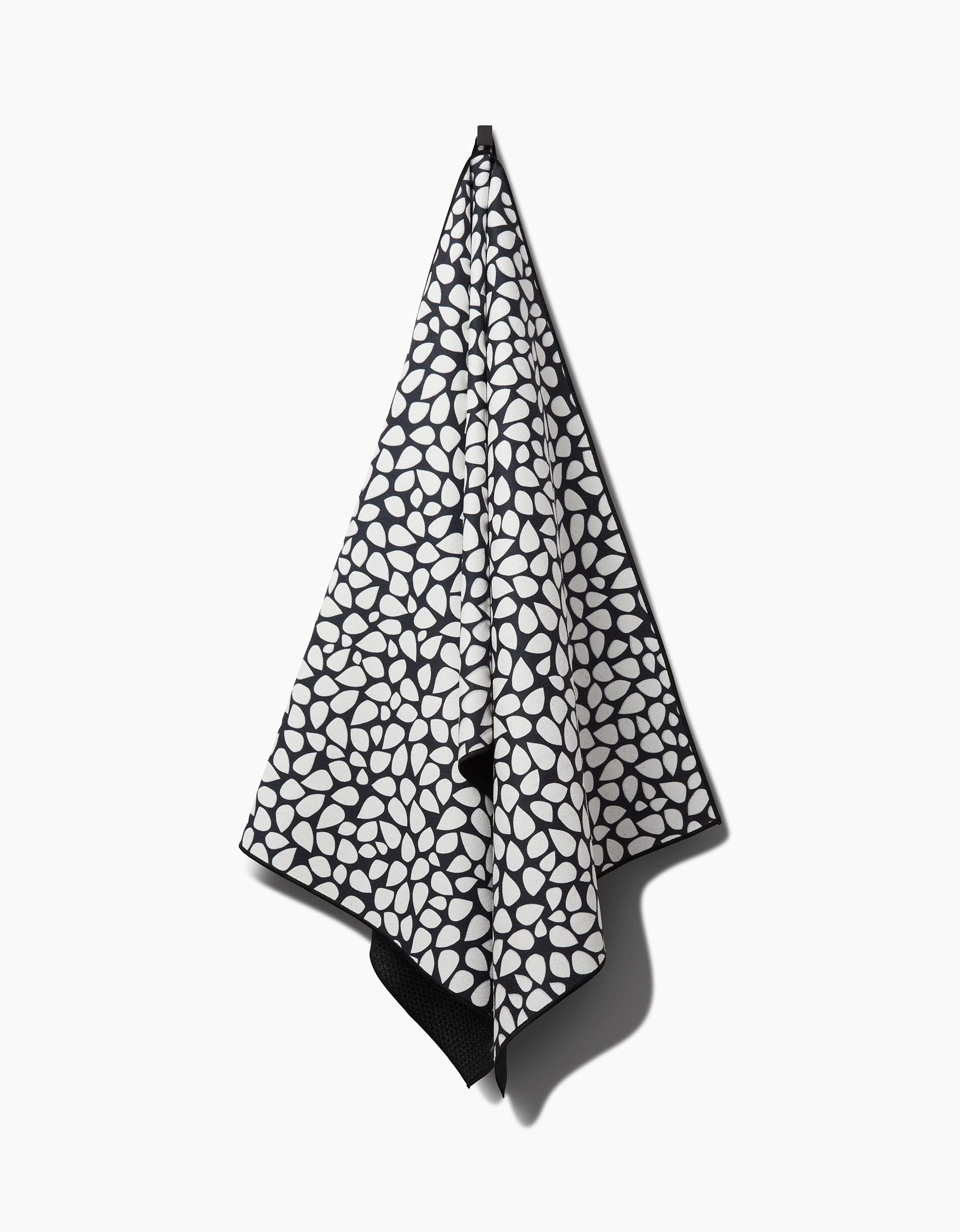 The Pebbles non-slip yoga towel by Marina Solodka features a black and white abstract oval pattern and hangs on a hook against a plain white background.