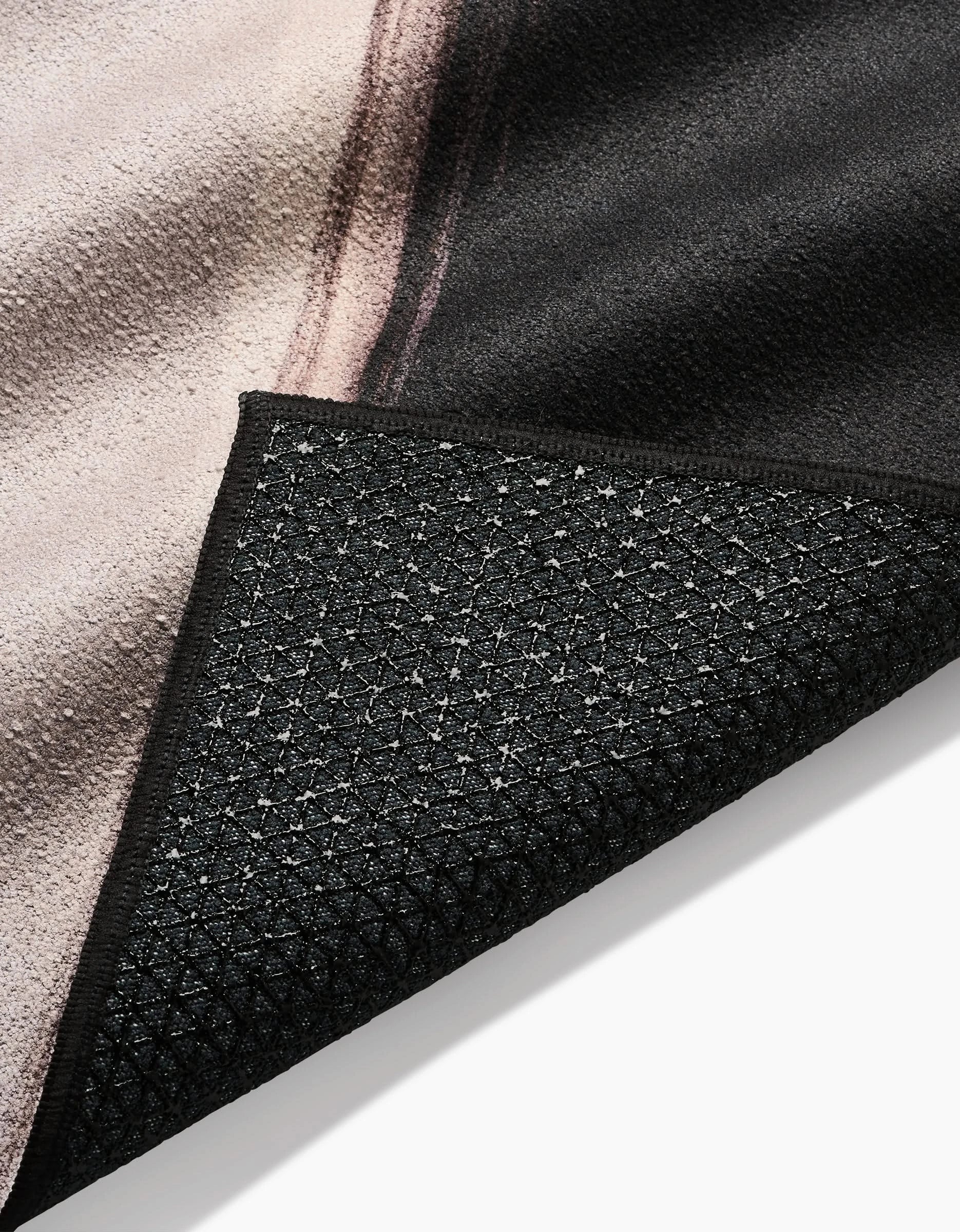 A close-up of Rhythm by Jennifer Janesko shows the textured, slip-resistant yoga towel-style black backing and part of the patterned front in black, beige, and brown.