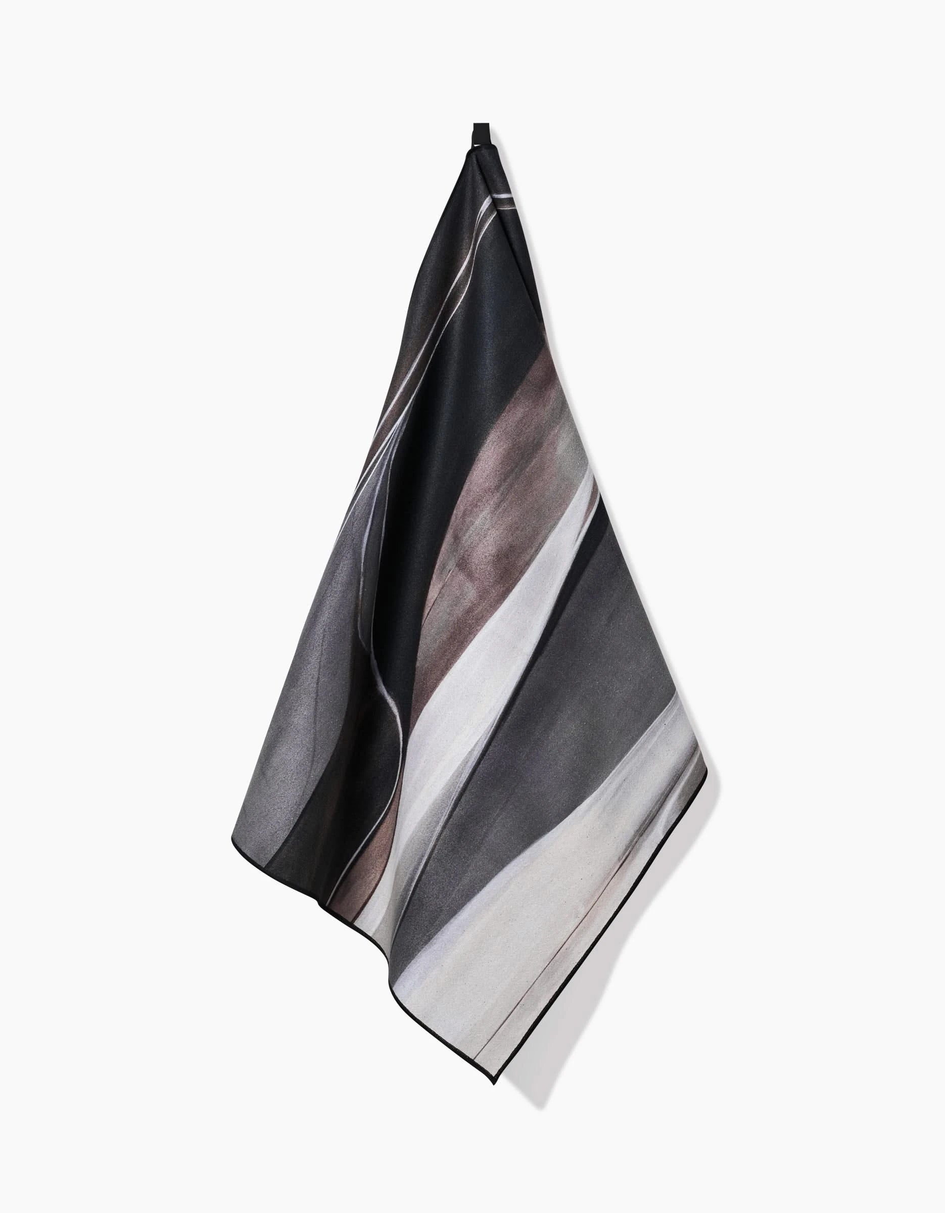 The Seduction recycled yoga towel by Jennifer Janesko, featuring a modern abstract pattern in black, gray, and white, hangs on a white wall.