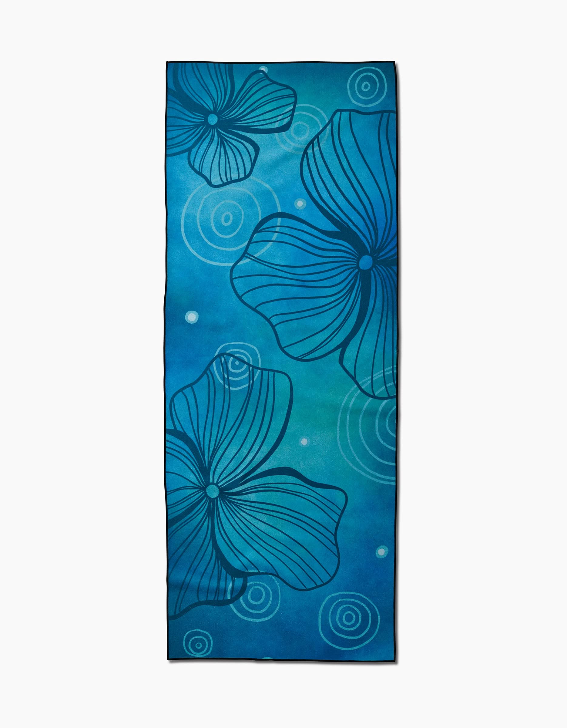 The Serenity yoga towel by Blissful Flamingo is a rectangular, blue, slip-resistant mat with large dark blue abstract floral designs and swirling circular patterns in the background.