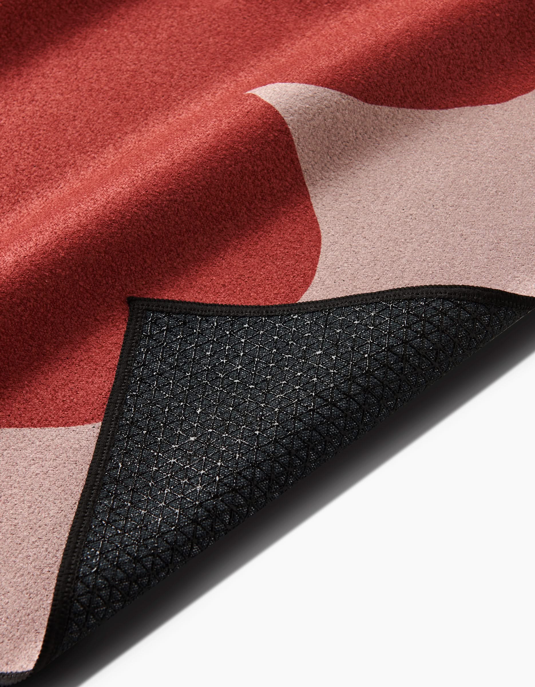A close-up of the Smoketree rug by PrintedPlant, featuring an abstract red and pink design on recycled material, with a black textured slip-resistant backing; one corner is folded to display both sides.