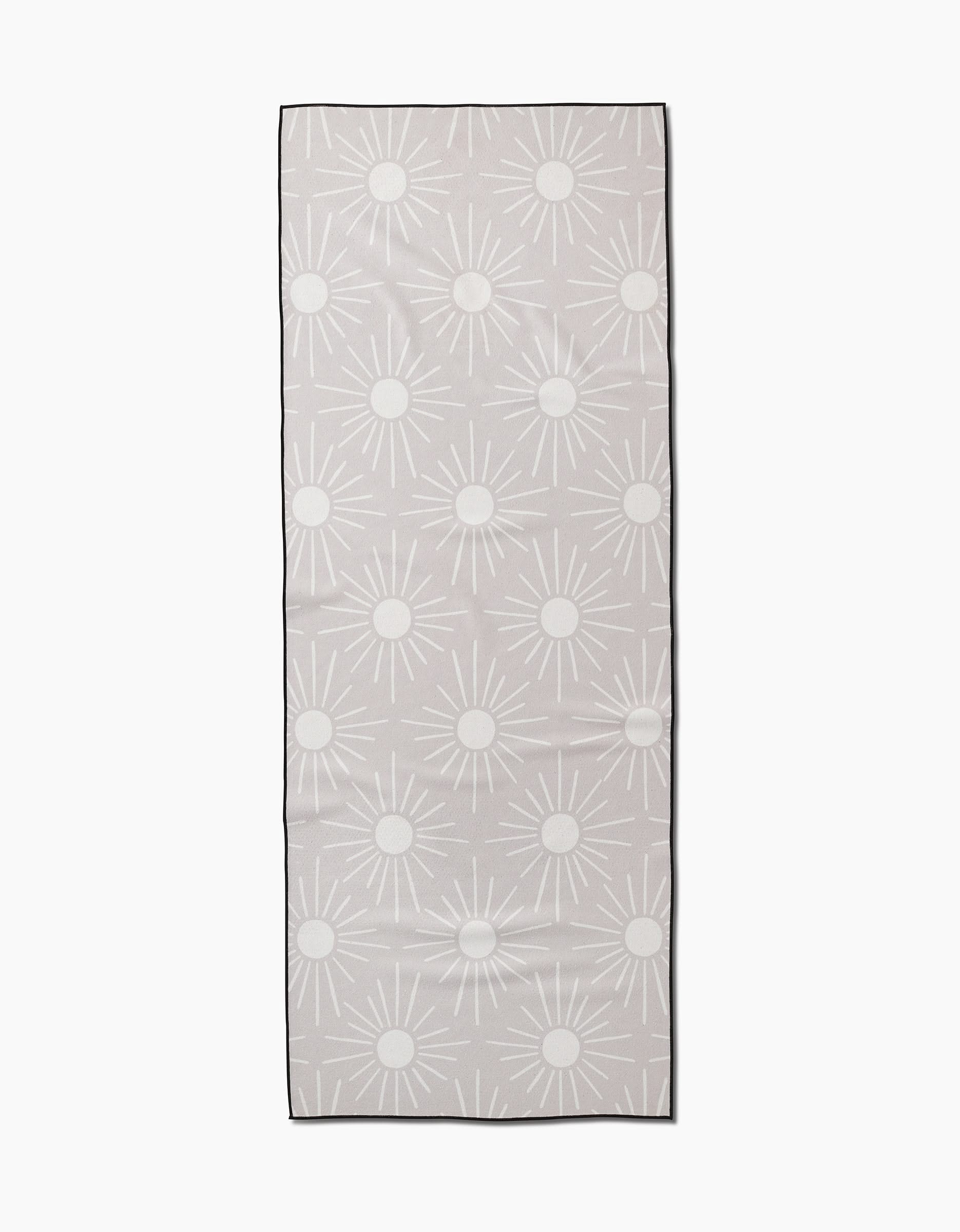 The Sunny Geo yoga towel by Hufton Studio is a rectangular beige towel featuring a repeating pattern of white sun shapes with circular centers and radiating lines on a plain background.