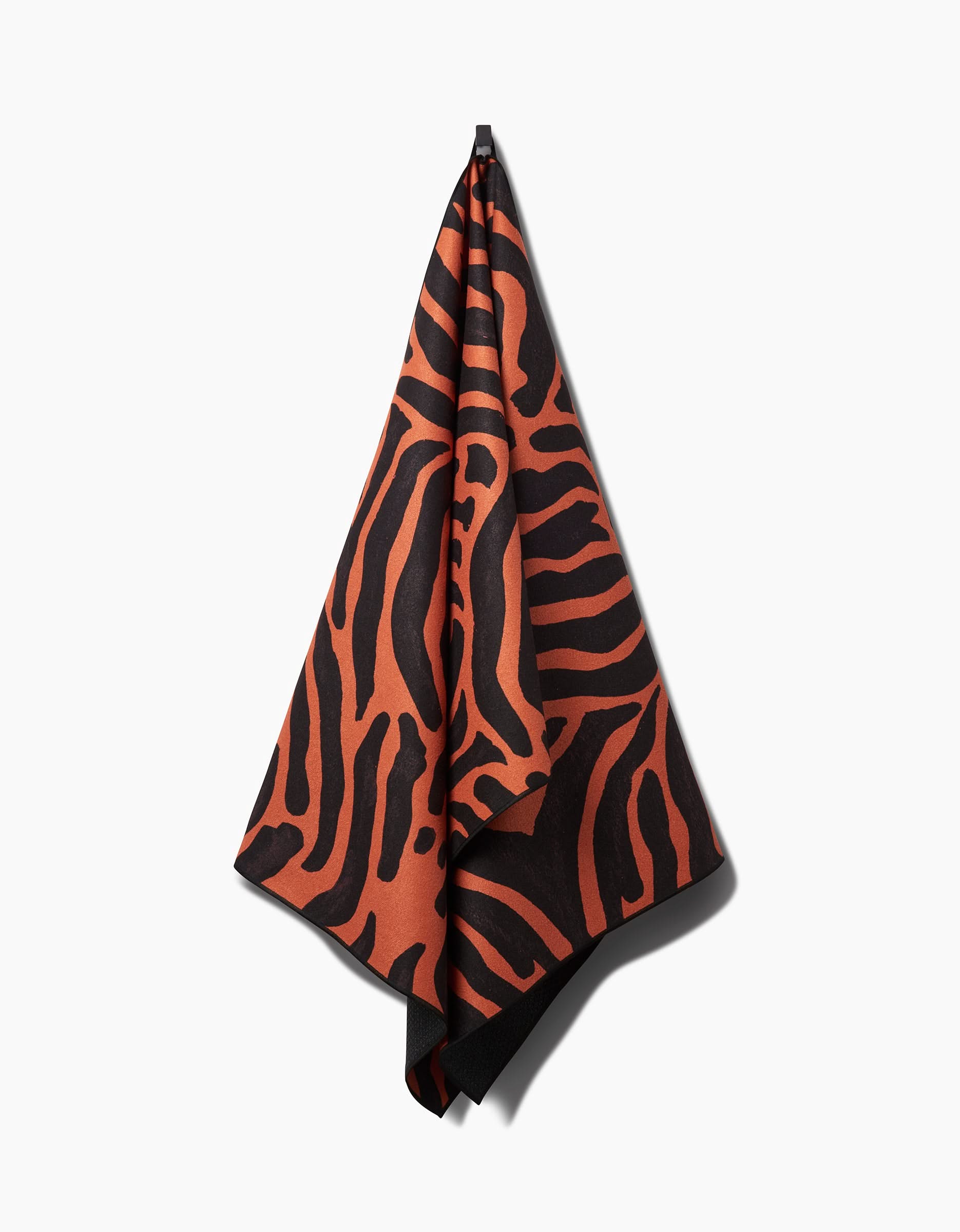 A GEOMETRY Tiger yoga towel featuring an orange and black zebra stripe design hangs on a hook against a plain white background. The towel offers slip-resistance for added stability during your yoga sessions.