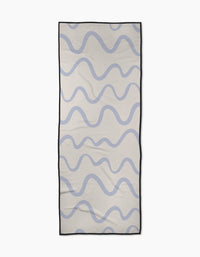 The Wavy Stripe in Blue yoga towel by Teri the Butter is a rectangular, recycled towel featuring wavy blue lines on a light beige background with a thin black border.