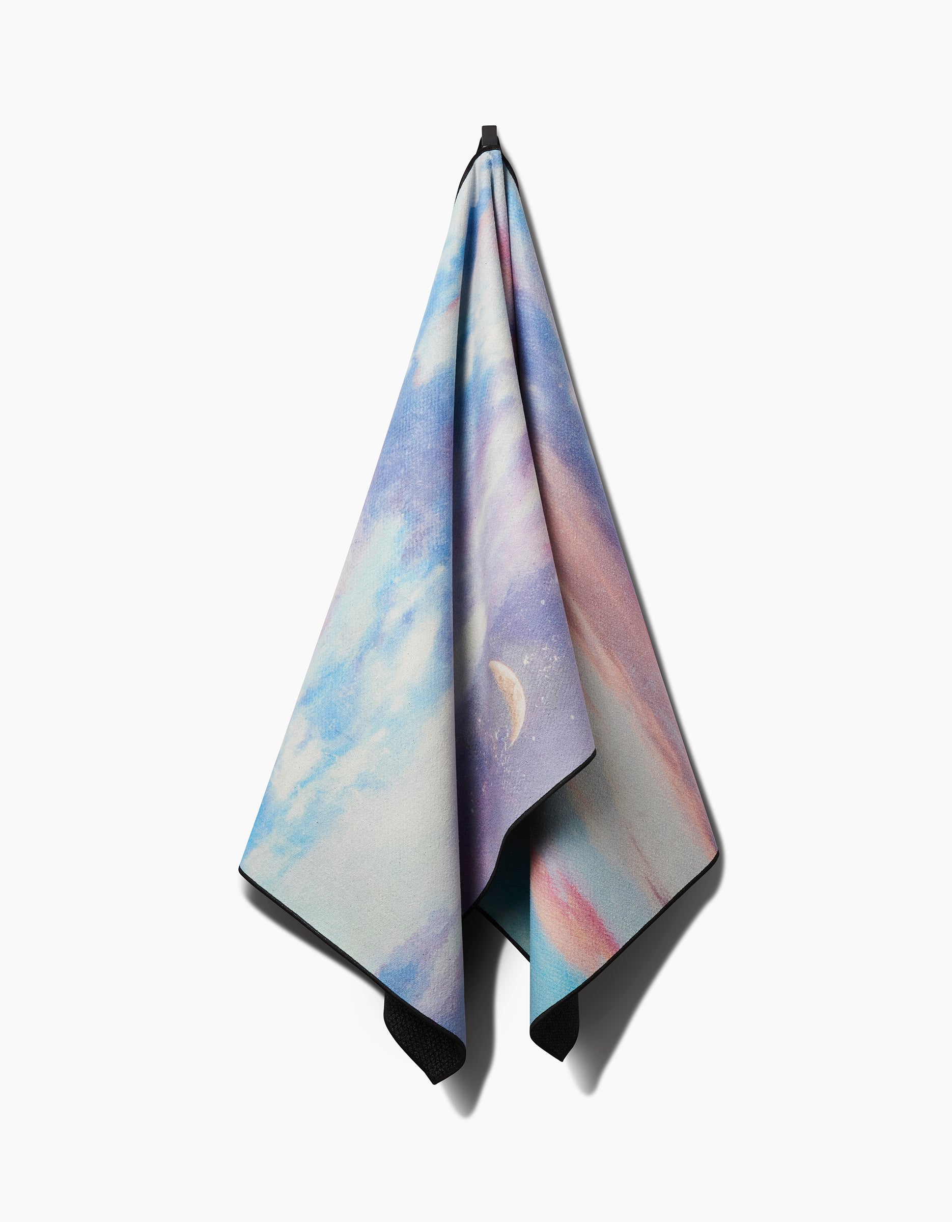 The When I Close My Eyes yoga towel by Stefanie Bales hangs on a hook, featuring clouds, a crescent moon, and pastel blue, purple, and pink shades on a white background.