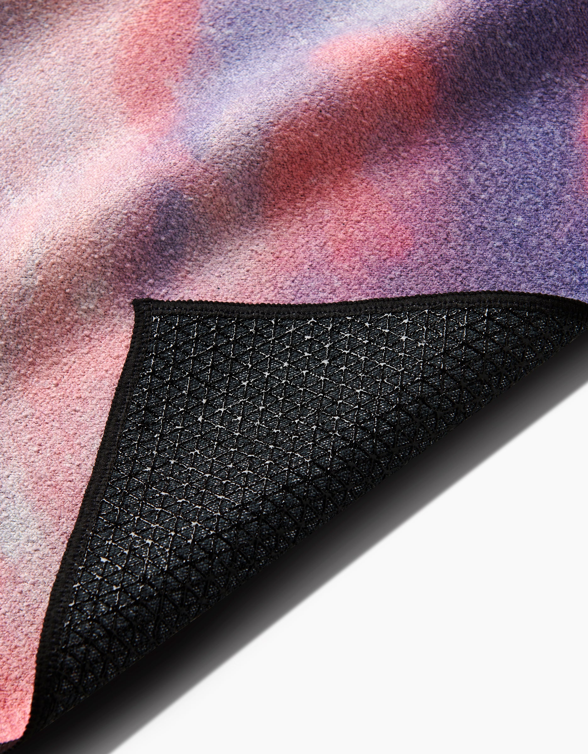 A close-up of the Stefanie Bales When I Close My Eyes yoga towel shows its soft, pink-purple-red gradient surface and a flipped corner revealing the black, grid-patterned non-slip underside.