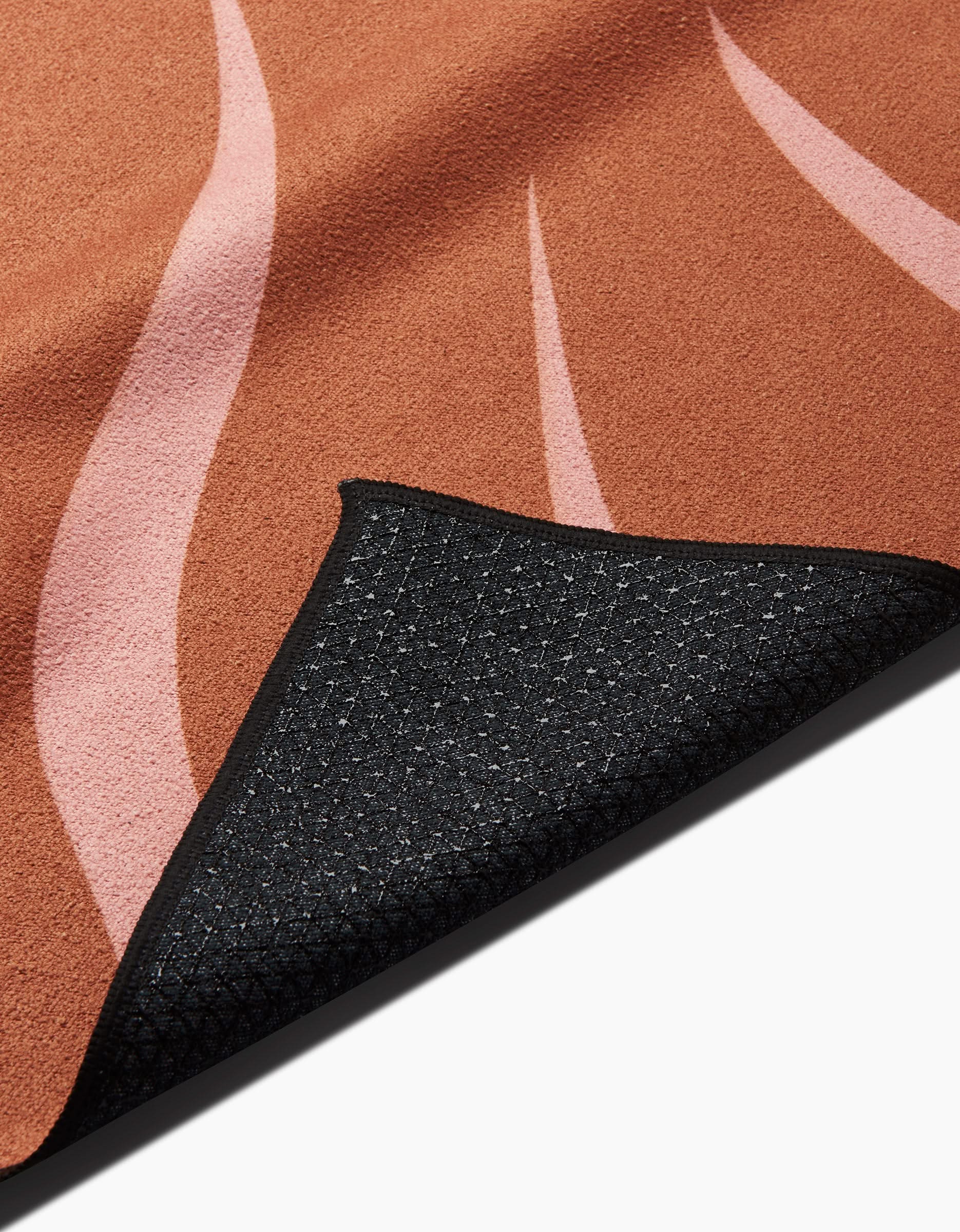 A close-up of the You are ENOUGH rug by Arielle Estoria, featuring a reddish-brown background with soft pink wavy lines. A lifted corner reveals the black non-slip silicone grip grid backing.