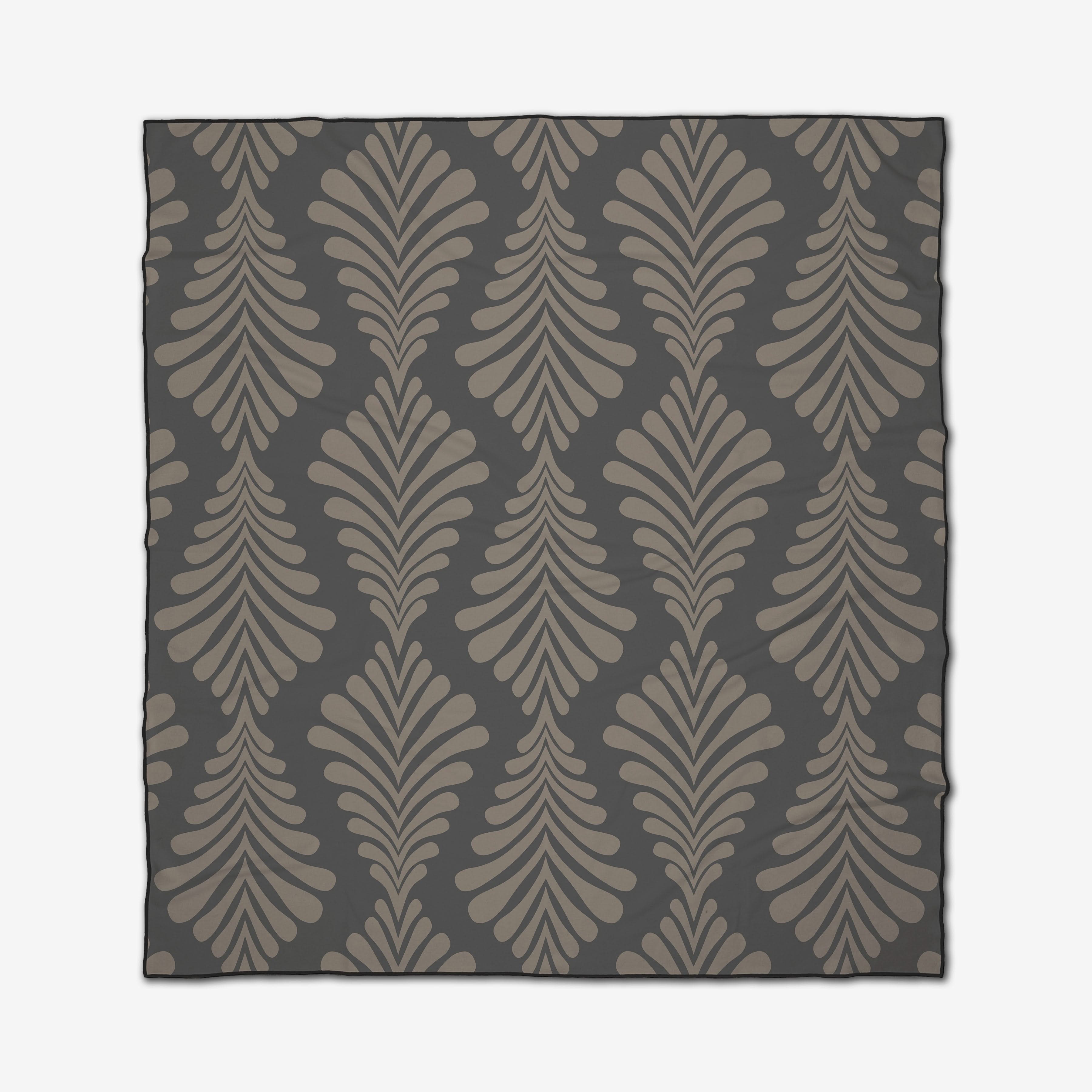 The GEOMETRY Dark Neutrals is a quick-drying beach blanket with a repeating pattern of stylized curved leaf shapes in taupe and beige on a dark gray background.