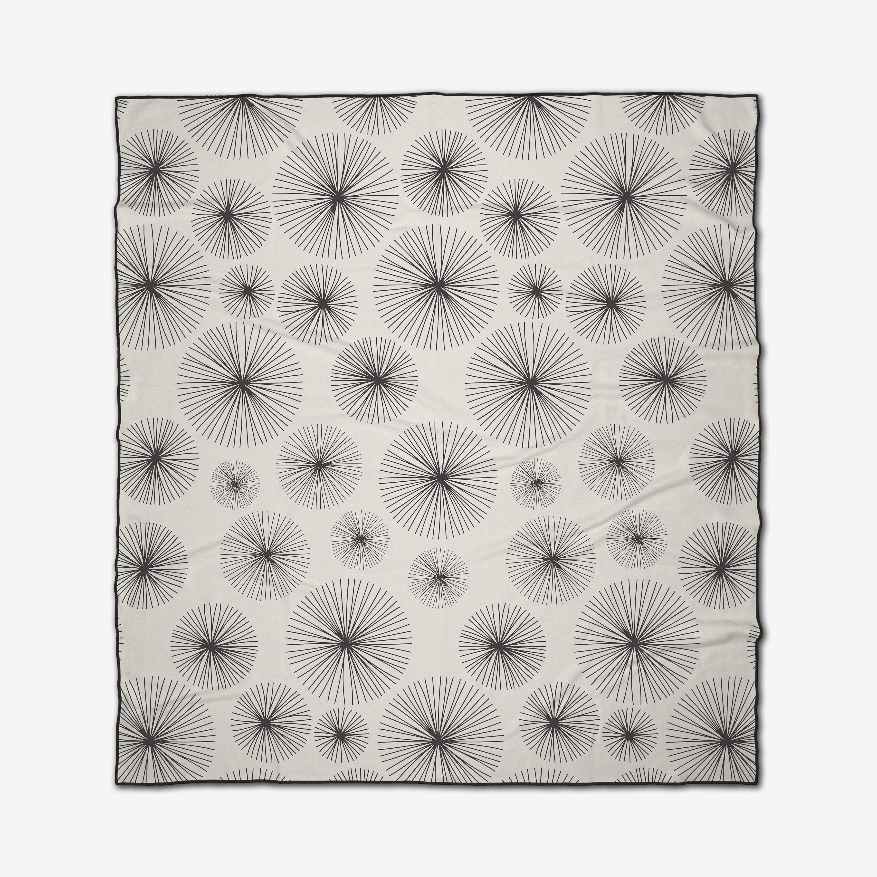The GEOMETRY Sky Party is a rectangular white micro-loop beach blanket with evenly spaced black radial starburst patterns of varying sizes and a thin black border.