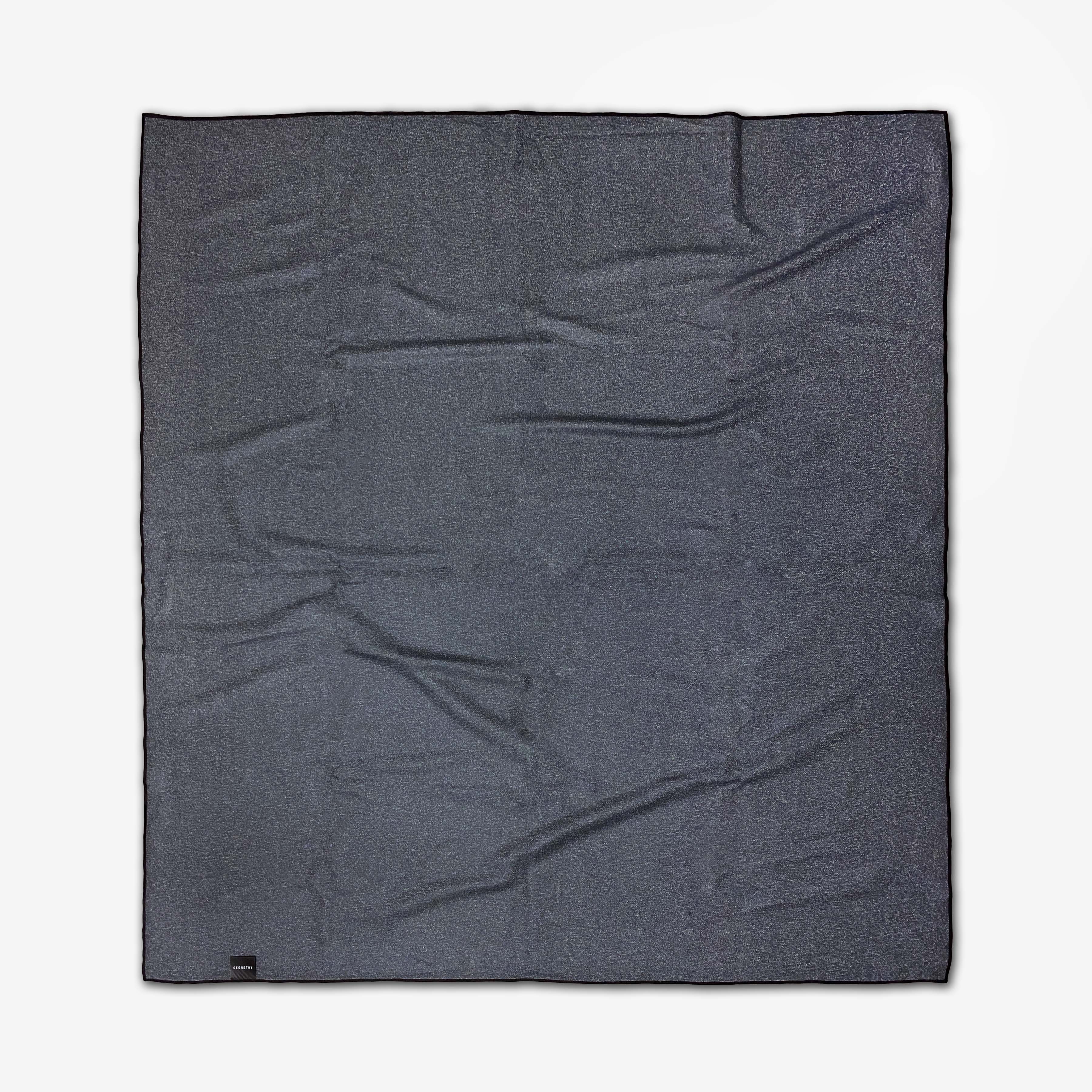 The GEOMETRY Palm Branches is a dark gray rectangular beach blanket made from quick-drying recycled material, shown with visible wrinkles and laid flat on a white background.