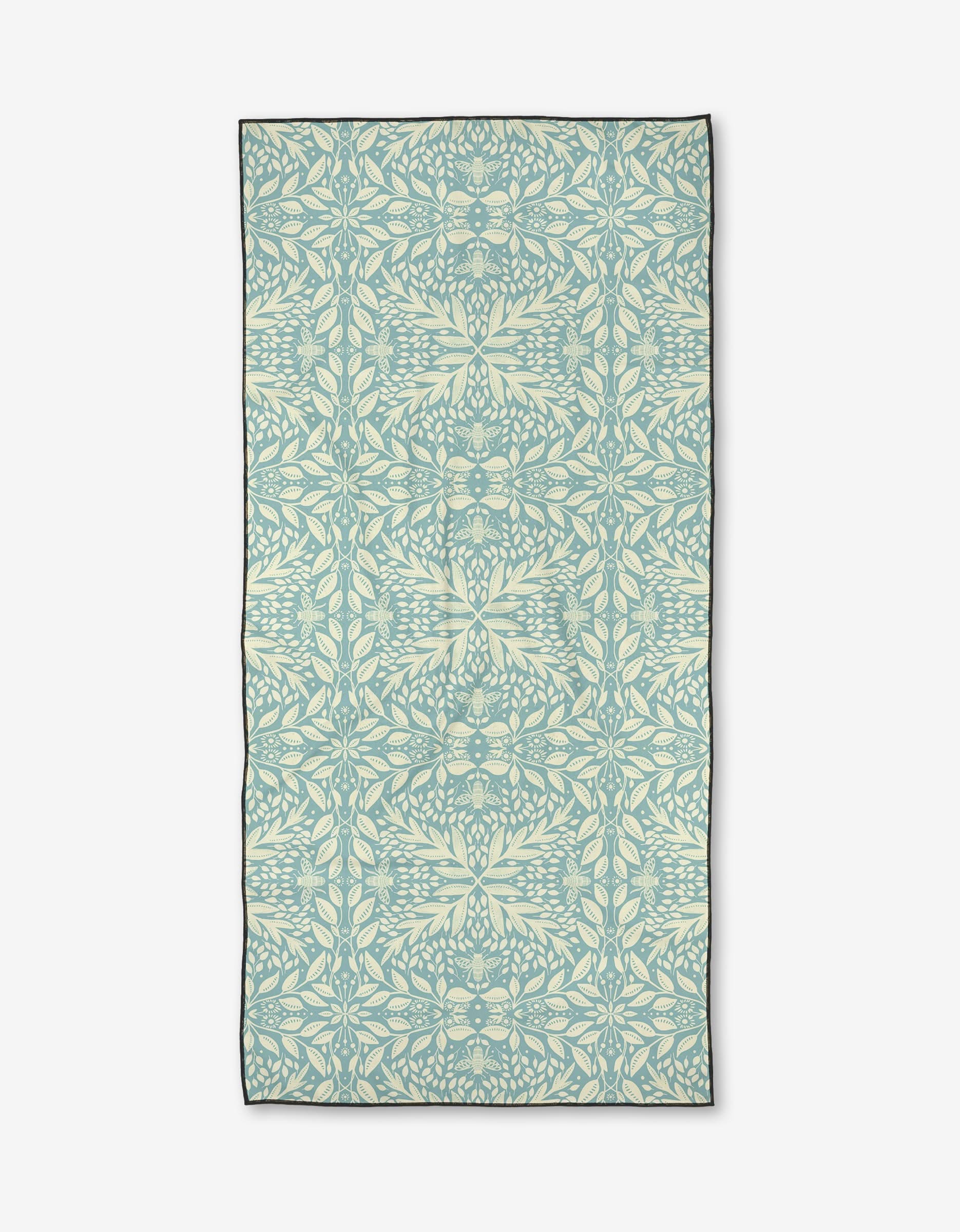 Bee Magic by Katie OShea is a rectangular micro-loop beach towel made from recycled materials, showcasing a pale blue and cream symmetrical leaf and vine pattern in an intricate botanical design on a white background.