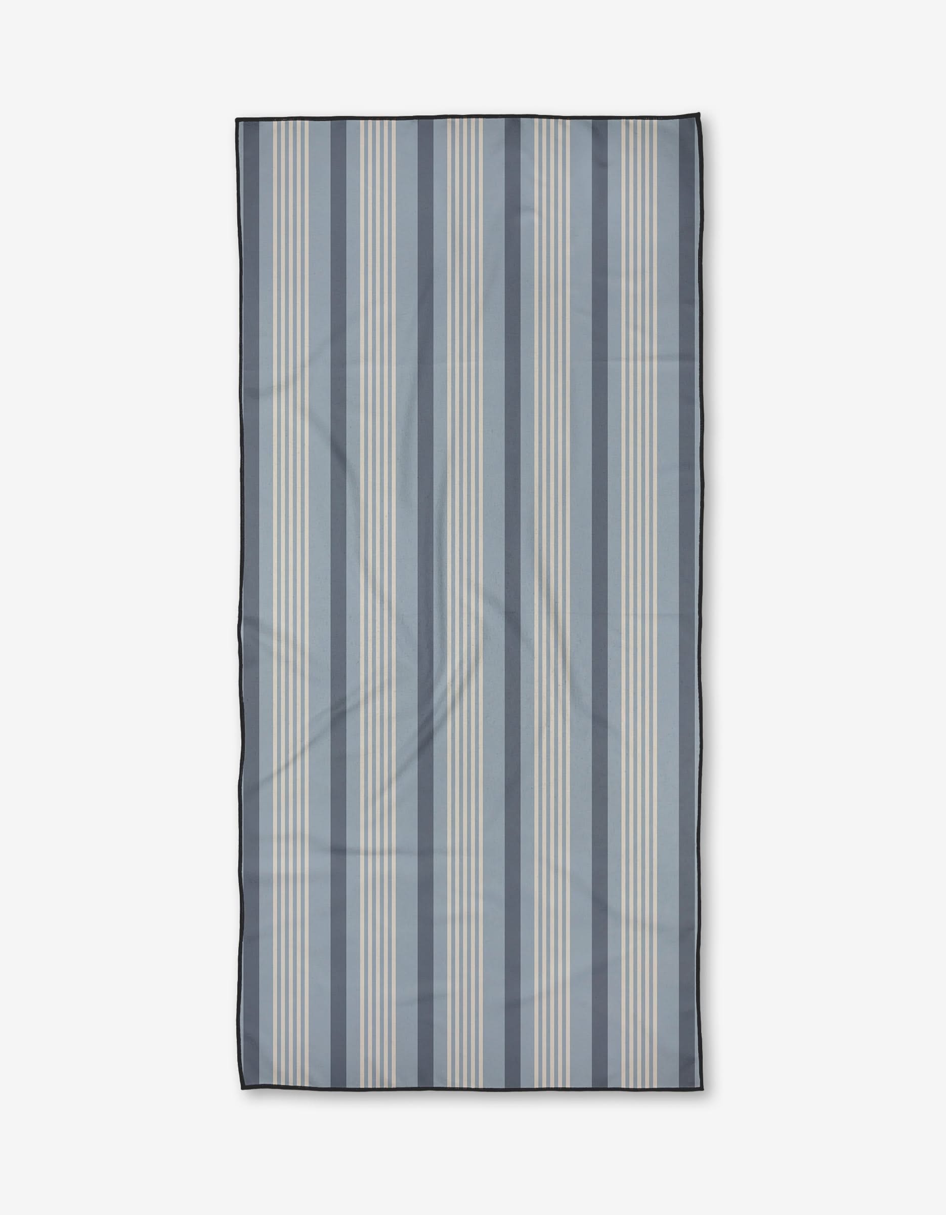 The Colleen beach towel by Becki Owens features vertical blue and light beige stripes on white, finished with a dark border. Made from quick-drying recycled materials for both convenience and sustainability.