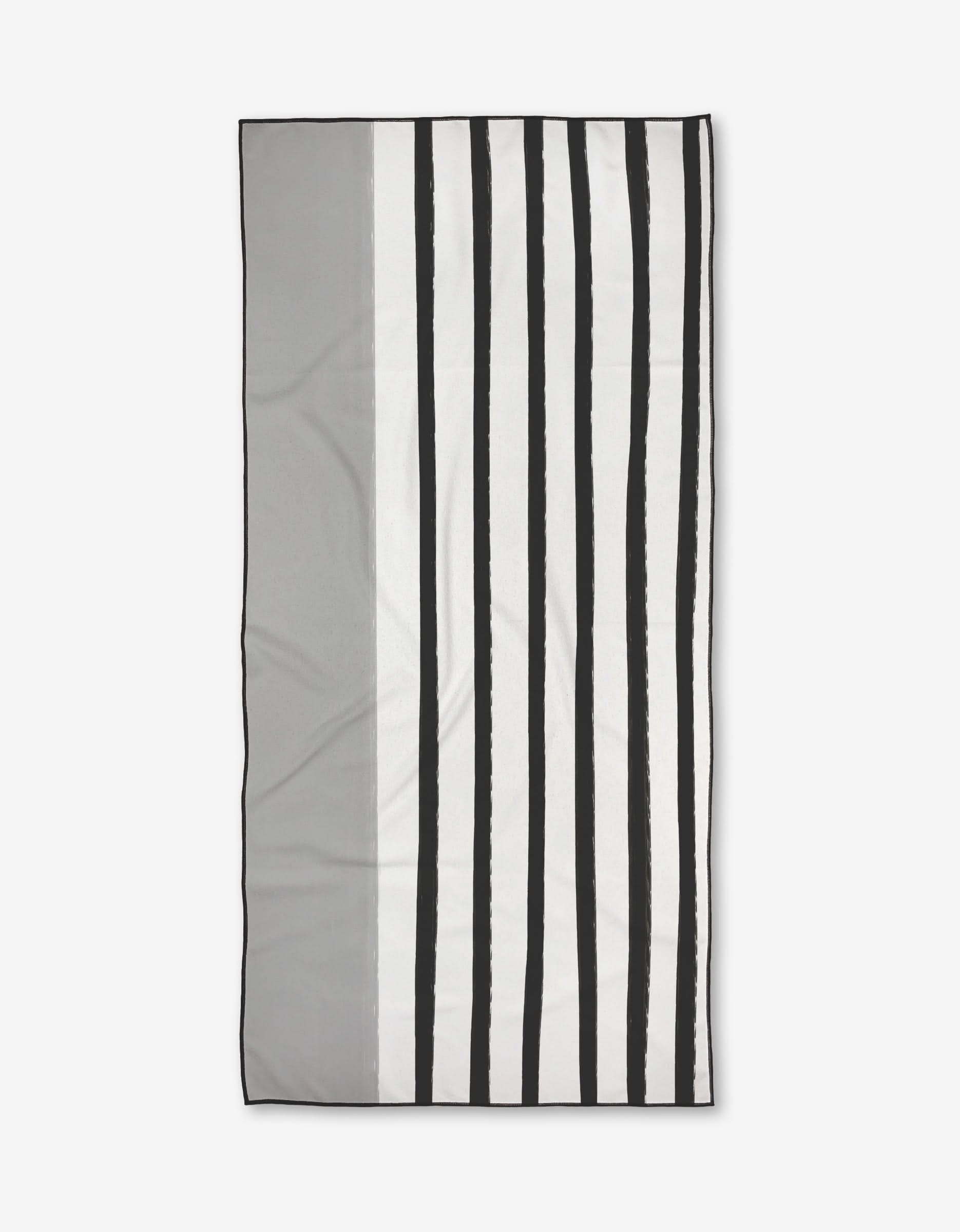 The Dawn beach towel by Kailee Wright is rectangular with a minimalist design—vertical black and white stripes on the right, solid gray on the left. Made from quick-drying recycled materials, its pictured against a plain white background.
