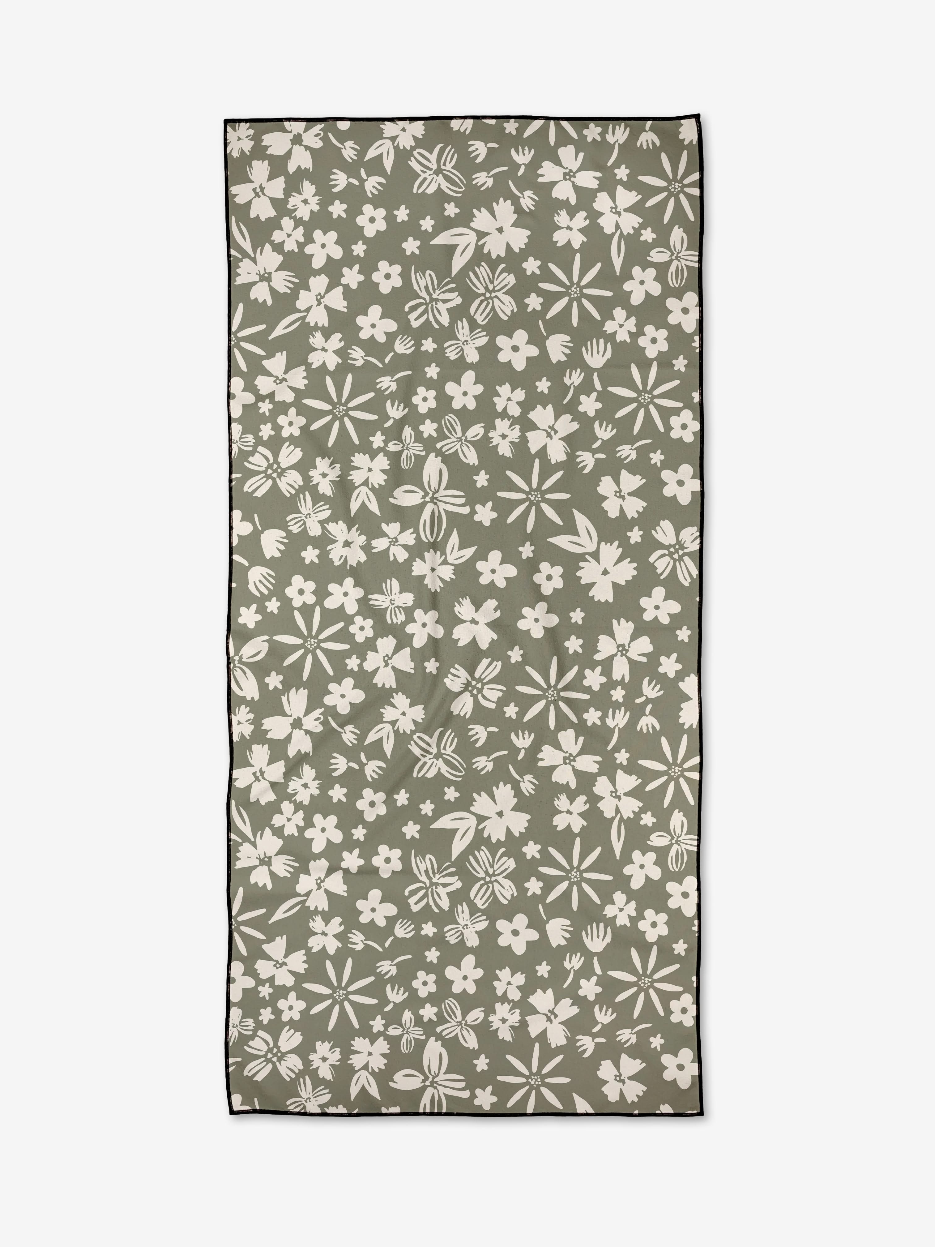 The Flourish Gardens towel by Hufton Studio is a rectangular, olive-green, quick-drying piece featuring a white floral pattern with various sized flowers and leaves, and finished with a thin black border around the edges.