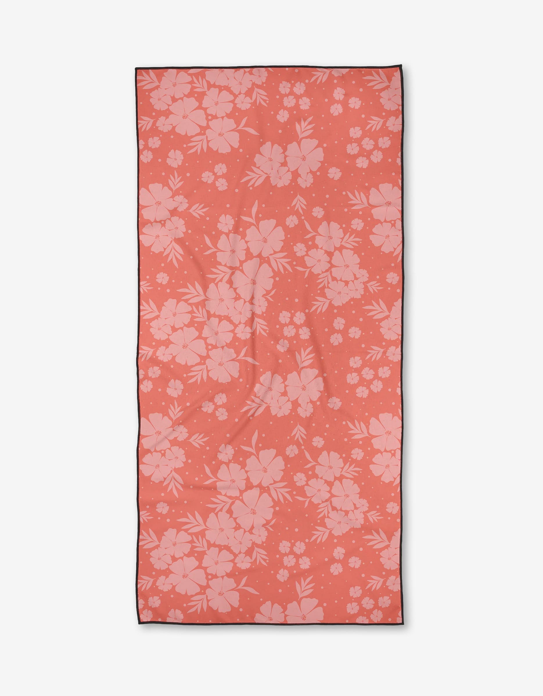 The Open Fields beach towel by Charlie Rowan Designs is rectangular, coral-colored, quick-drying, and features a light pink floral pattern of assorted flowers and leaves.