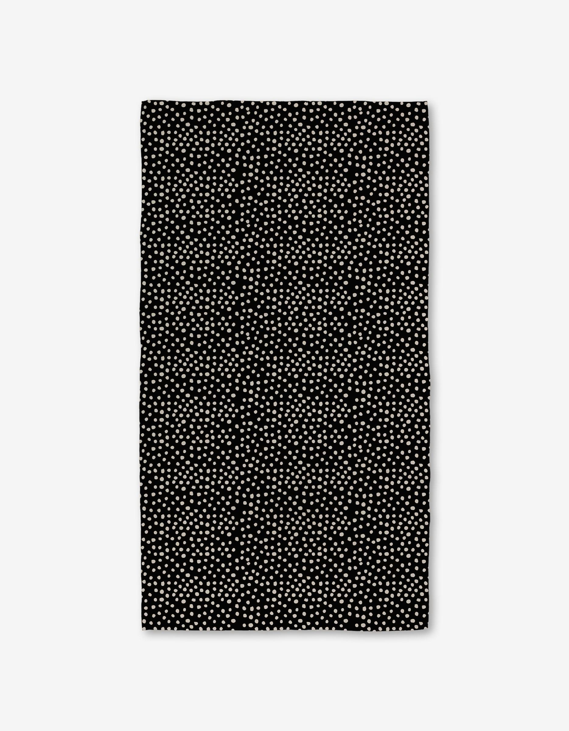 The Dotty Black Luxe Bath Towel by GEOMETRY showcases evenly spaced small white dots on a rectangular black surface, made with ultra-absorbent Geoweave technology, displayed against a white background.