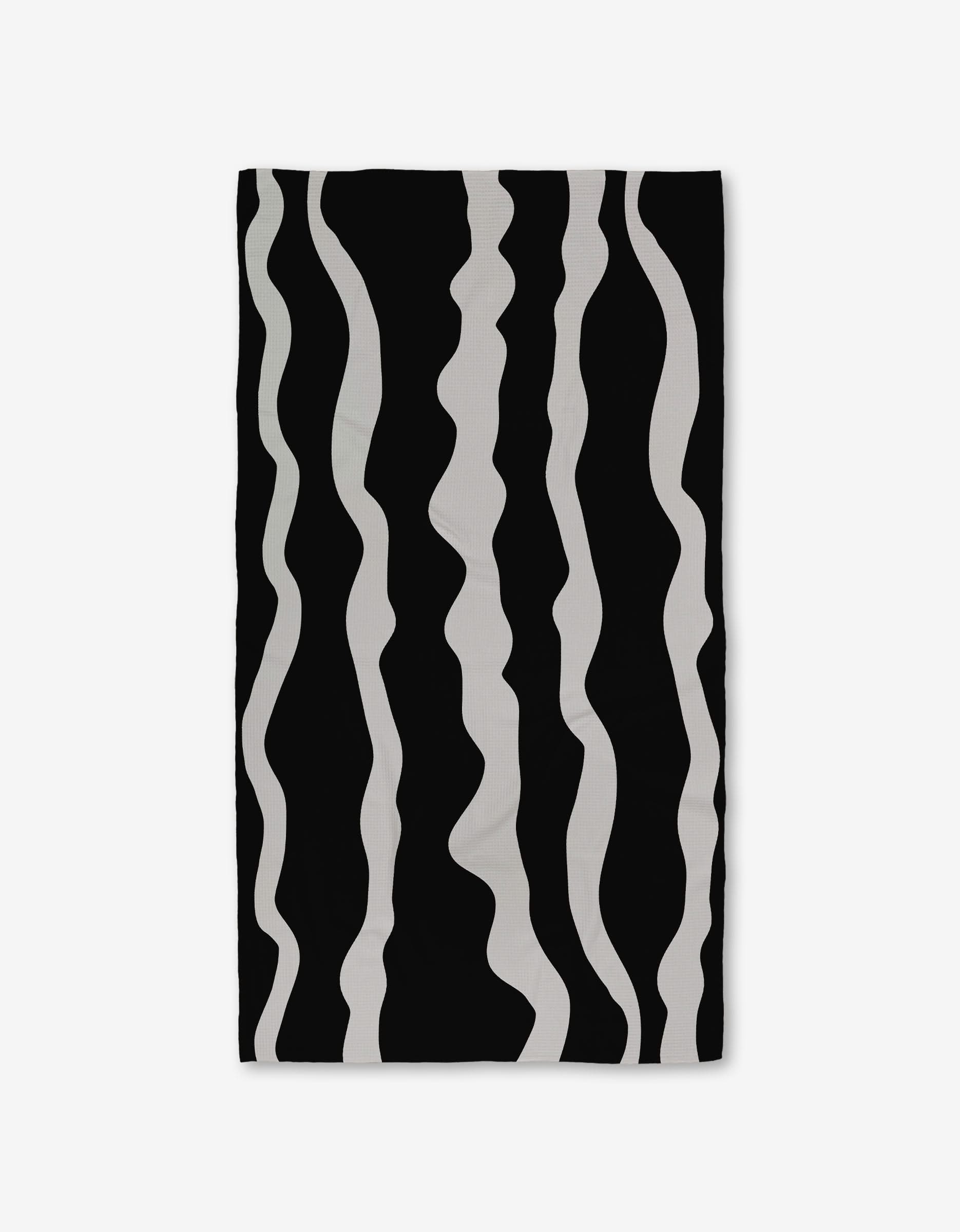 The GEOMETRY Ink Twist bath towel is made from recycled materials and features a black background with wavy, vertical white stripes of varying thickness for a stylish, ultra-absorbent finish.
