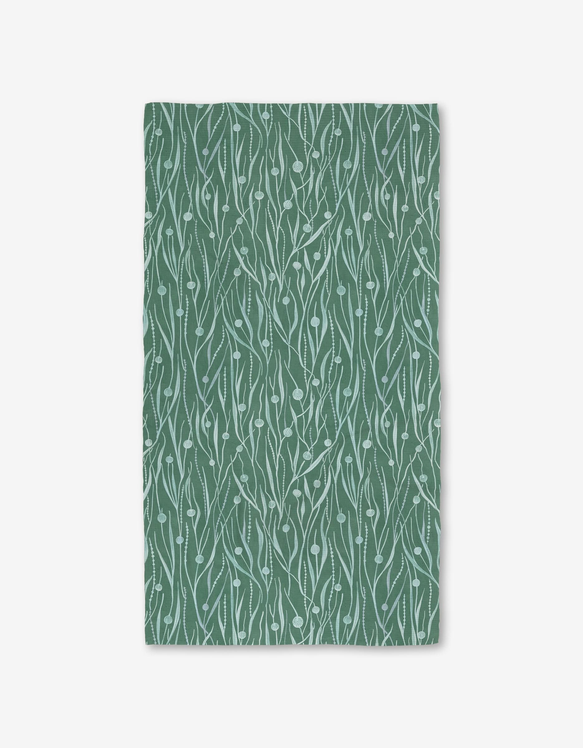 The Katie OShea Kelp Luxe Bath Towel is rectangular, green, and made from recycled materials. It features a white abstract botanical leaf-and-vine pattern and is photographed flat on a white background.