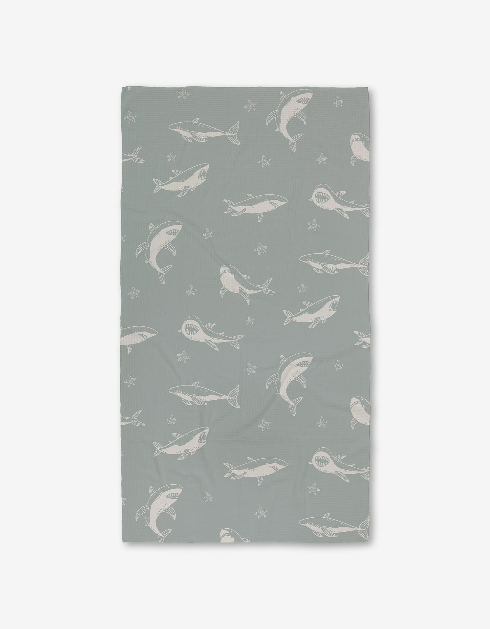 The Toothy Tales Luxe Bath Towel by Janna Sue Design features gray and white sharks with starfish on a light gray background. Made with Geoweave technology for exceptional softness and absorbency. Displayed against a plain white backdrop.