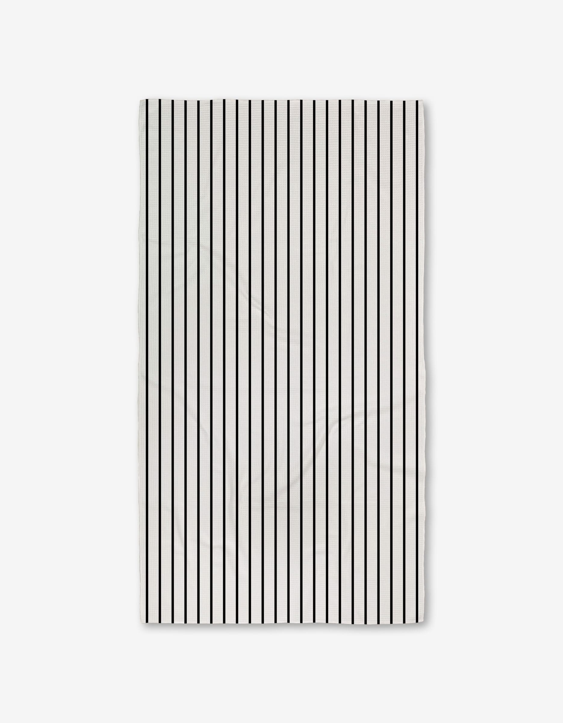 The White Linen towel by GEOMETRY is rectangular, white with evenly spaced vertical black stripes, crafted from ultra-absorbent recycled materials and shown against a plain light background.