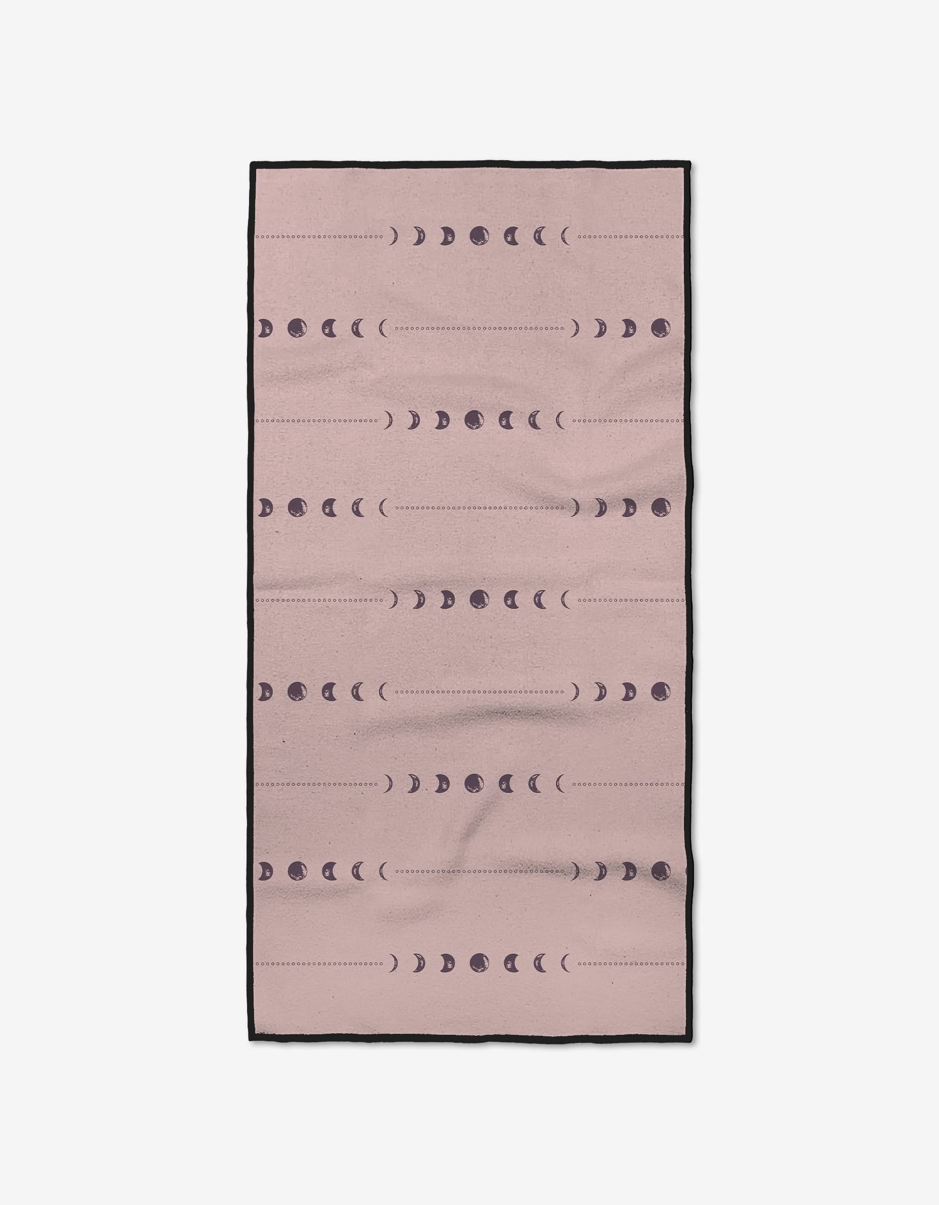 The Night Sky fitness towel by Ashley Celena is rectangular and pink with black edges, featuring dark purple moon phases in horizontal rows. Made from ultra-absorbent recycled materials, it’s stylish and eco-friendly.