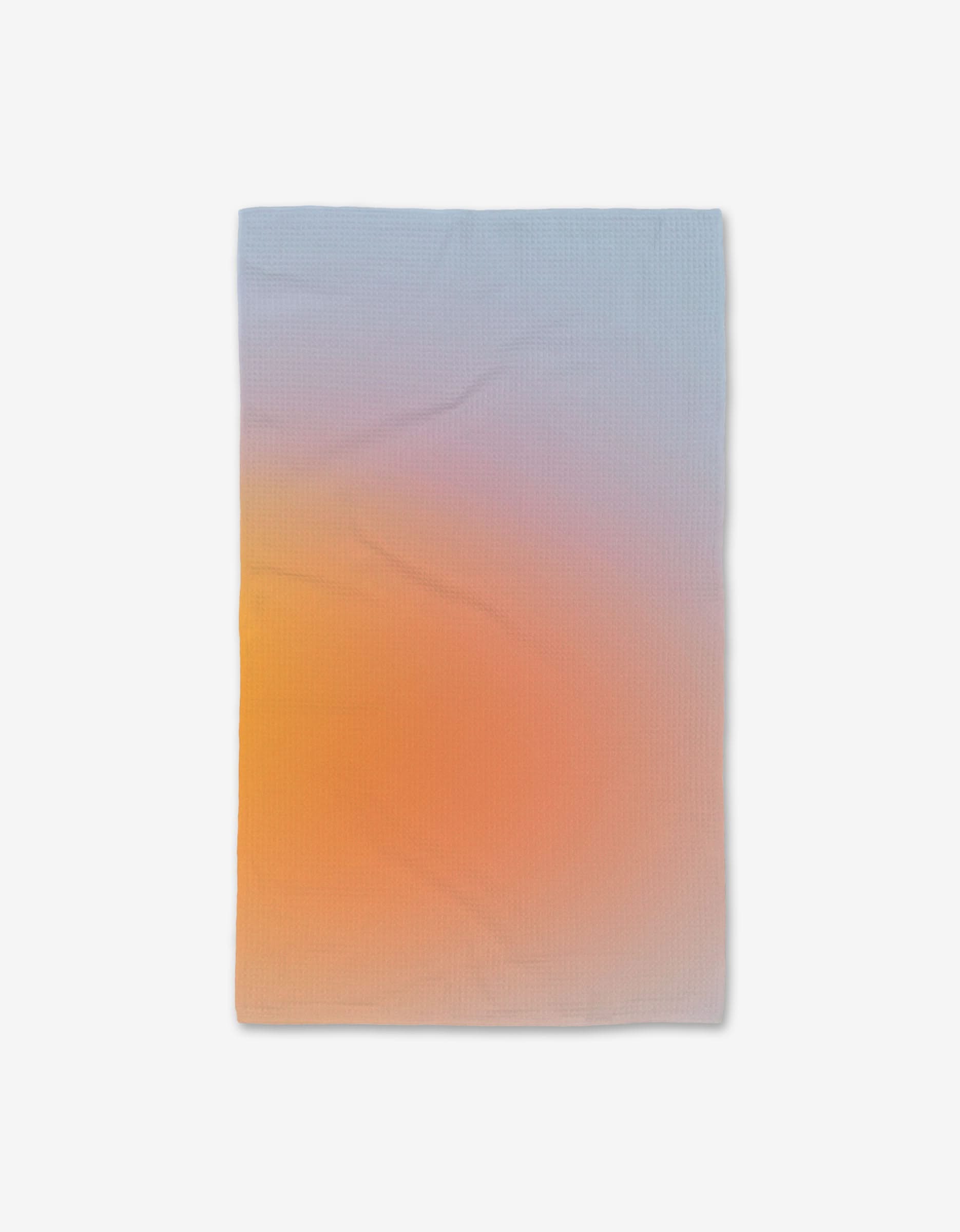 The GEOMETRY Aura blanket features a smooth gradient from light blue to soft orange and yellow, crafted with Geoweave technology for ultra-absorbency. Displayed on a white background.