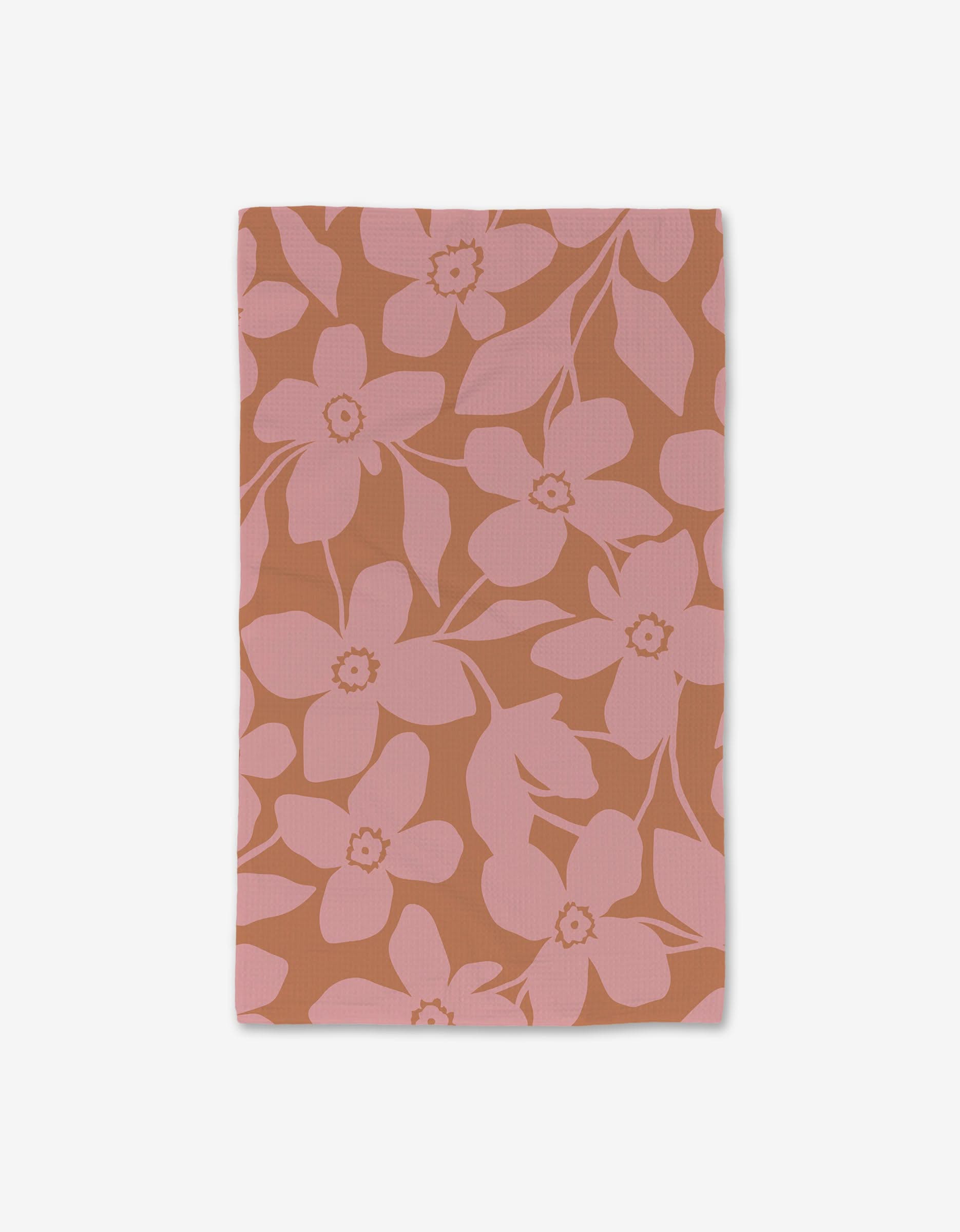 The GEOMETRY Big Fuchsia Flowers hand towel features a pink floral pattern with large blooms and leaves on a brownish-orange background. Ultra-absorbent, this luxe rectangular cloth is shown on a white surface.
