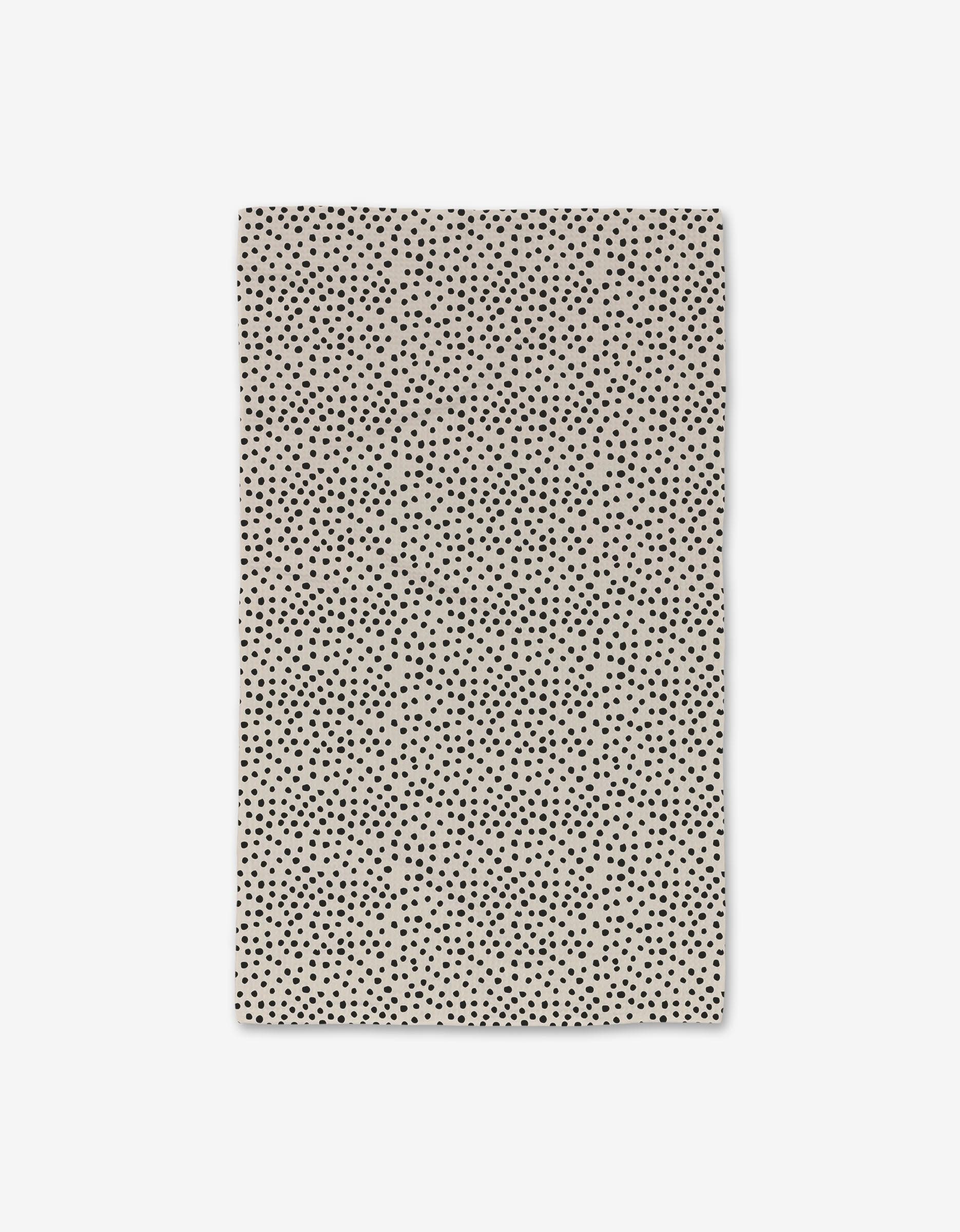 The GEOMETRY Dotty Tan Hand Towel features a rectangular beige design with an all-over pattern of small, irregular black polka dots. This ultra-absorbent towel combines elegance and practicality for everyday use. Displayed flat on a white background.