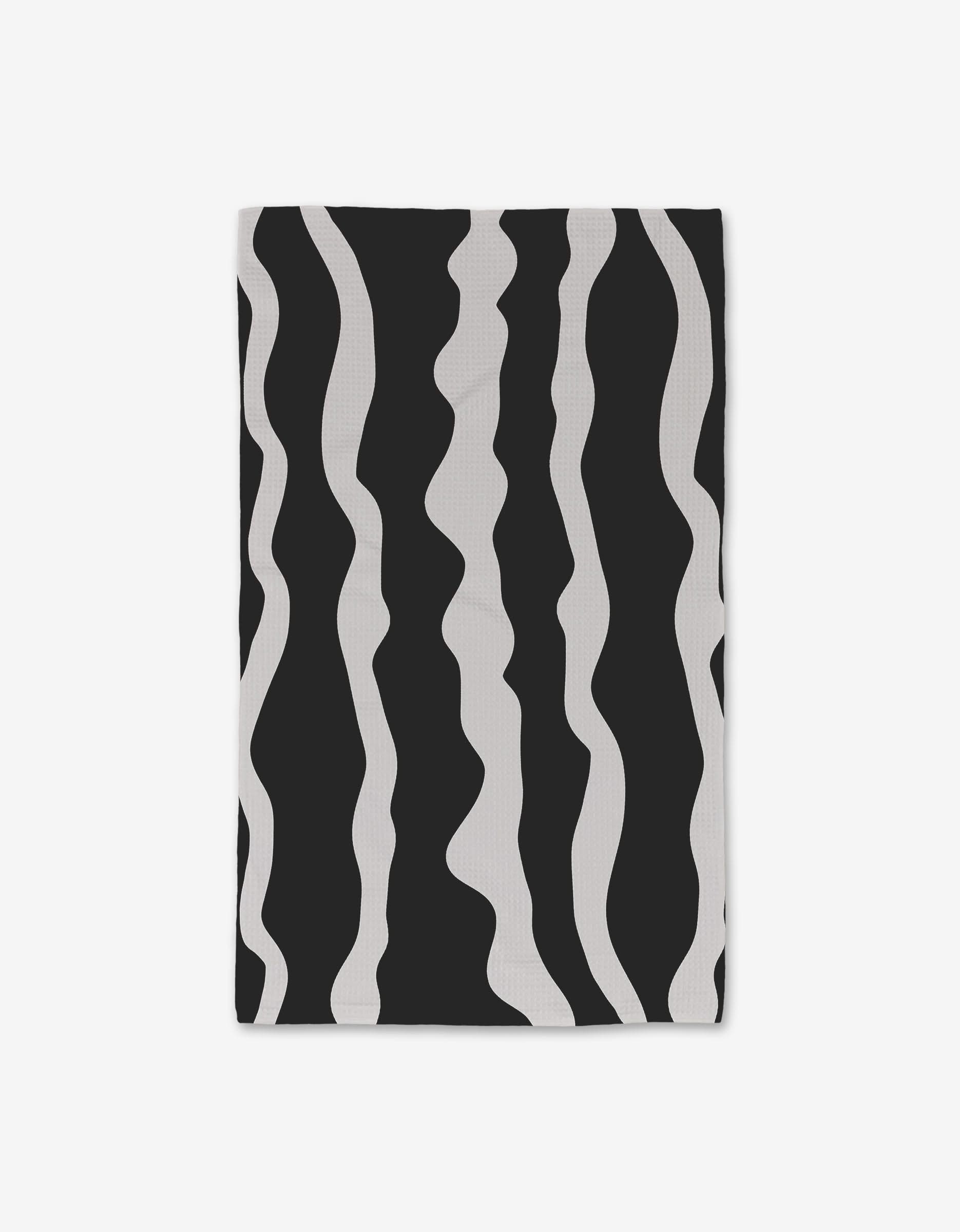 The GEOMETRY Ink Twist hand towel is rectangular, featuring a black background with irregular wavy white vertical stripes, and is crafted from ultra-absorbent recycled materials.