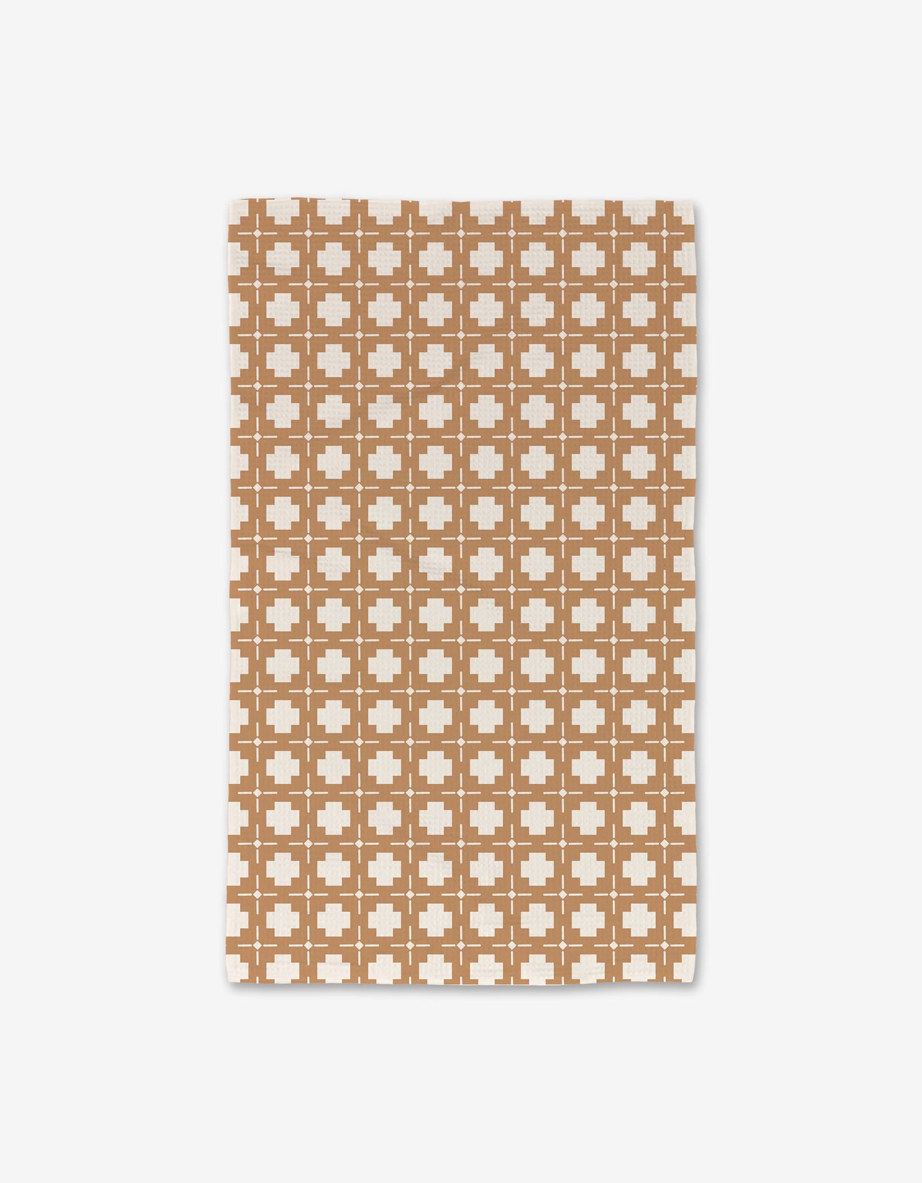 The Jackson blanket by Charlie Rowan Designs features a repeating white plus-sign pattern on a brown background, crafted from recycled materials with slightly irregular edges and shown laid flat on a white surface.
