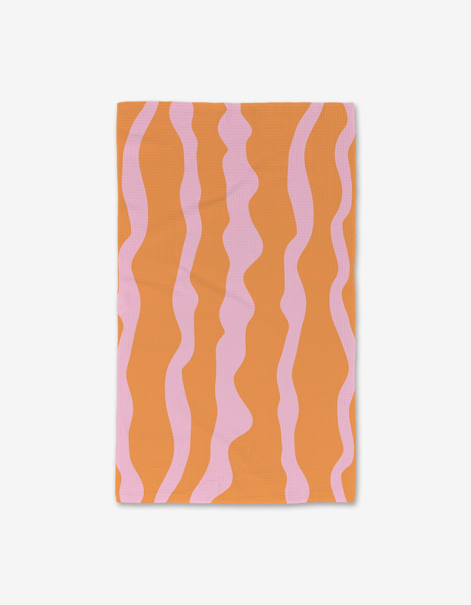 The GEOMETRY Tangerine Twist hand towel, made from recycled materials, features wavy pink vertical stripes on an orange background and is shown flat on a white surface.