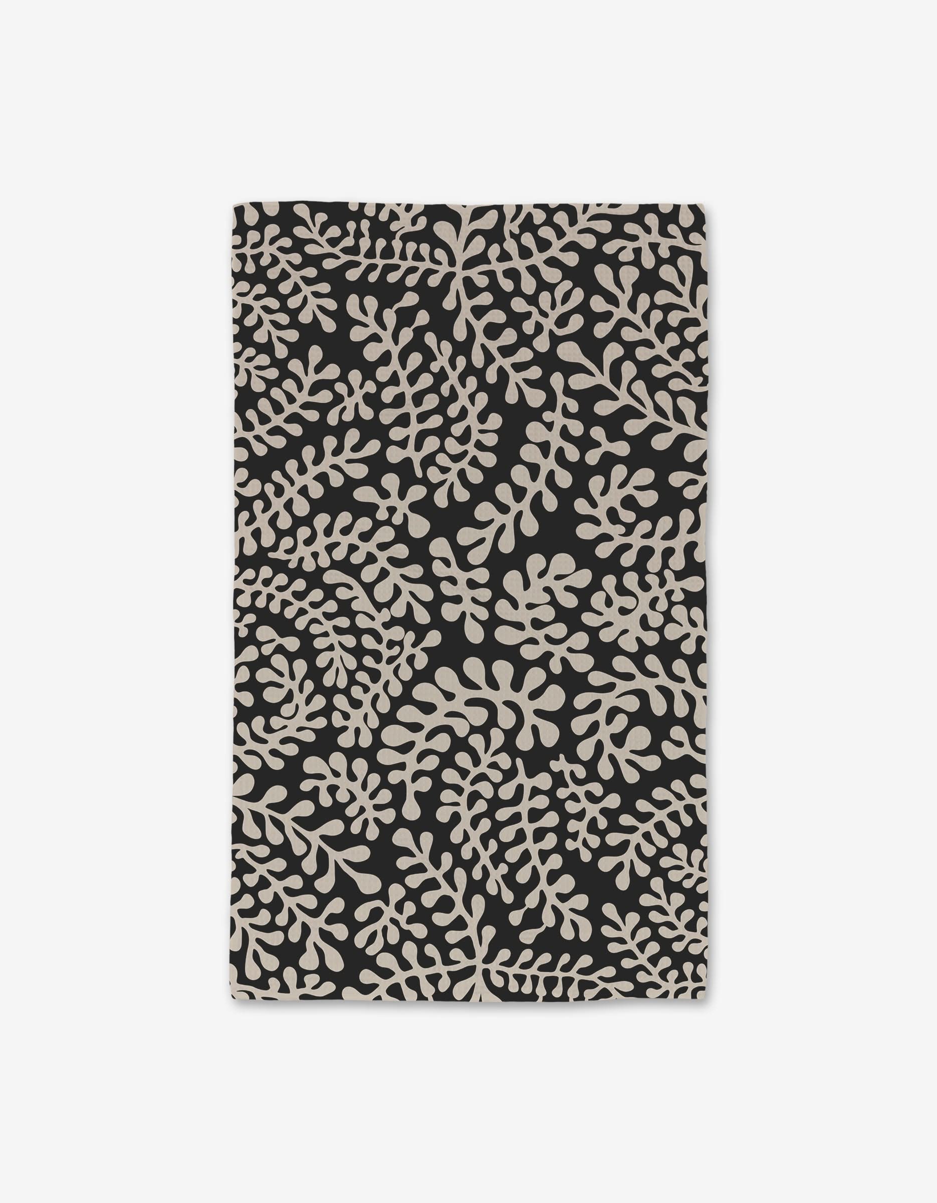 The Tangled hand towel by GEOMETRY features a black rectangular cloth with an abstract beige leafy pattern, crafted using Geoweave technology for ultra-absorbency—perfect as a luxe touch in any modern space.