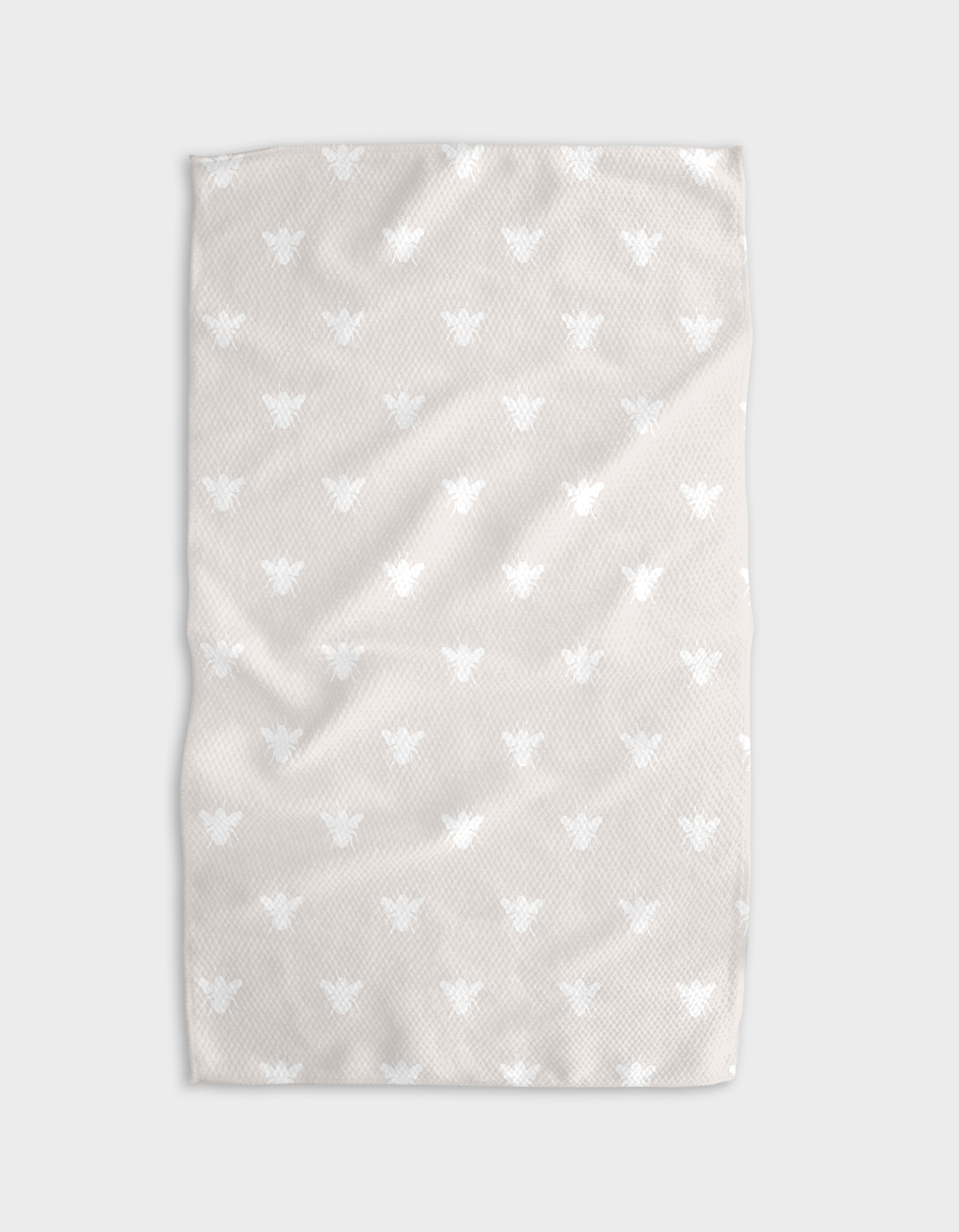The Buy Guide’s Queen Bee - Beige tea towel is crafted from recycled materials, featuring a soft beige color and a white bee pattern, shown gently folded with a textured look against a plain gray background.