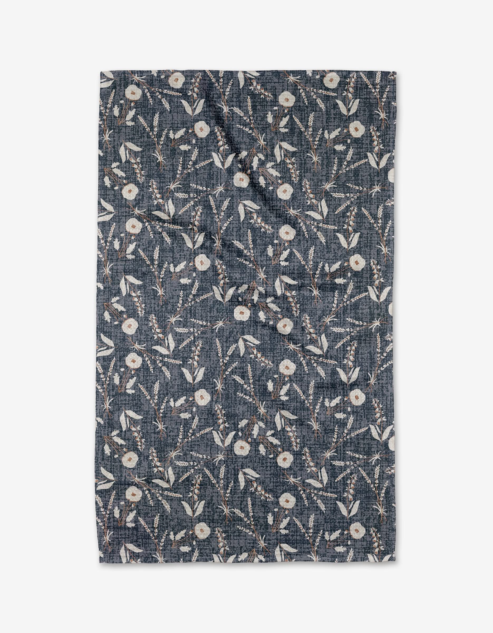 The Becki Owens Boyce Blue Tea Towel features a dark blue background with white flowers, green leaves, and thin branches evenly spread across its slightly wrinkled Geoweave fabric.