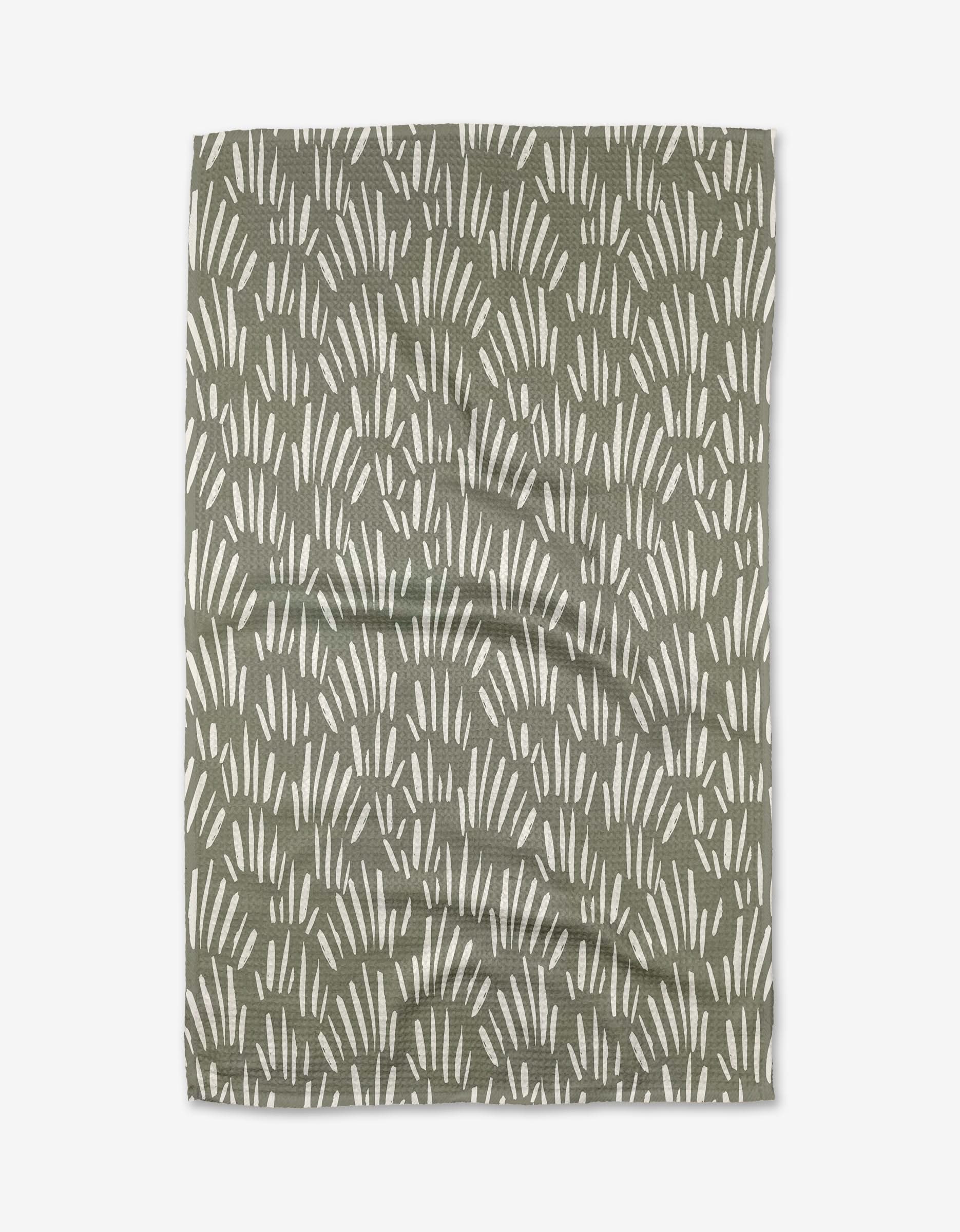 The Country Fields tea towel by Hufton Studio is made from green Geoweave fabric with a repeating pattern of white, curved lines resembling abstract grass or leaves. The towel is shown laid flat with slight wrinkles visible.