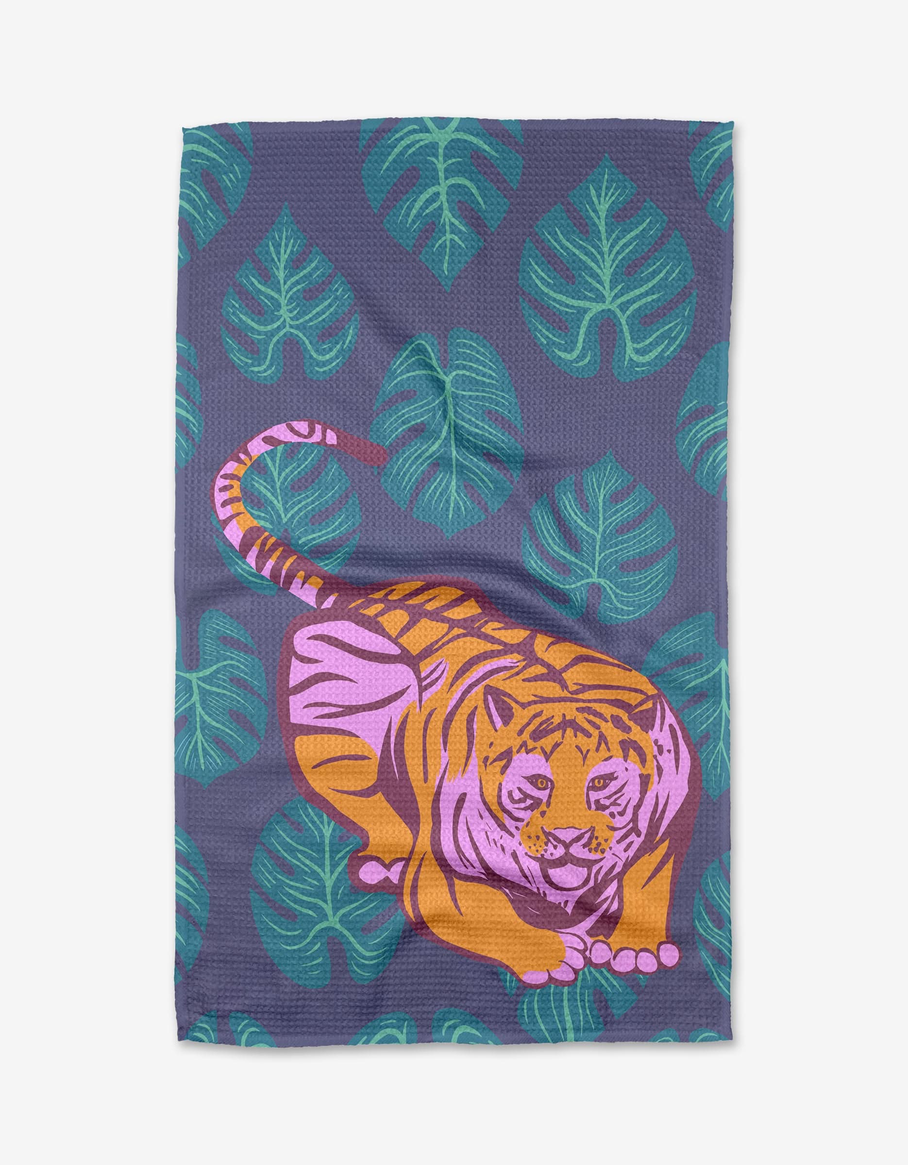 The Crouching Cat tea towel by Elisabeth Wing features an illustrated cat lounging among green tropical leaves on a dark purple background, and is crafted from recycled materials.