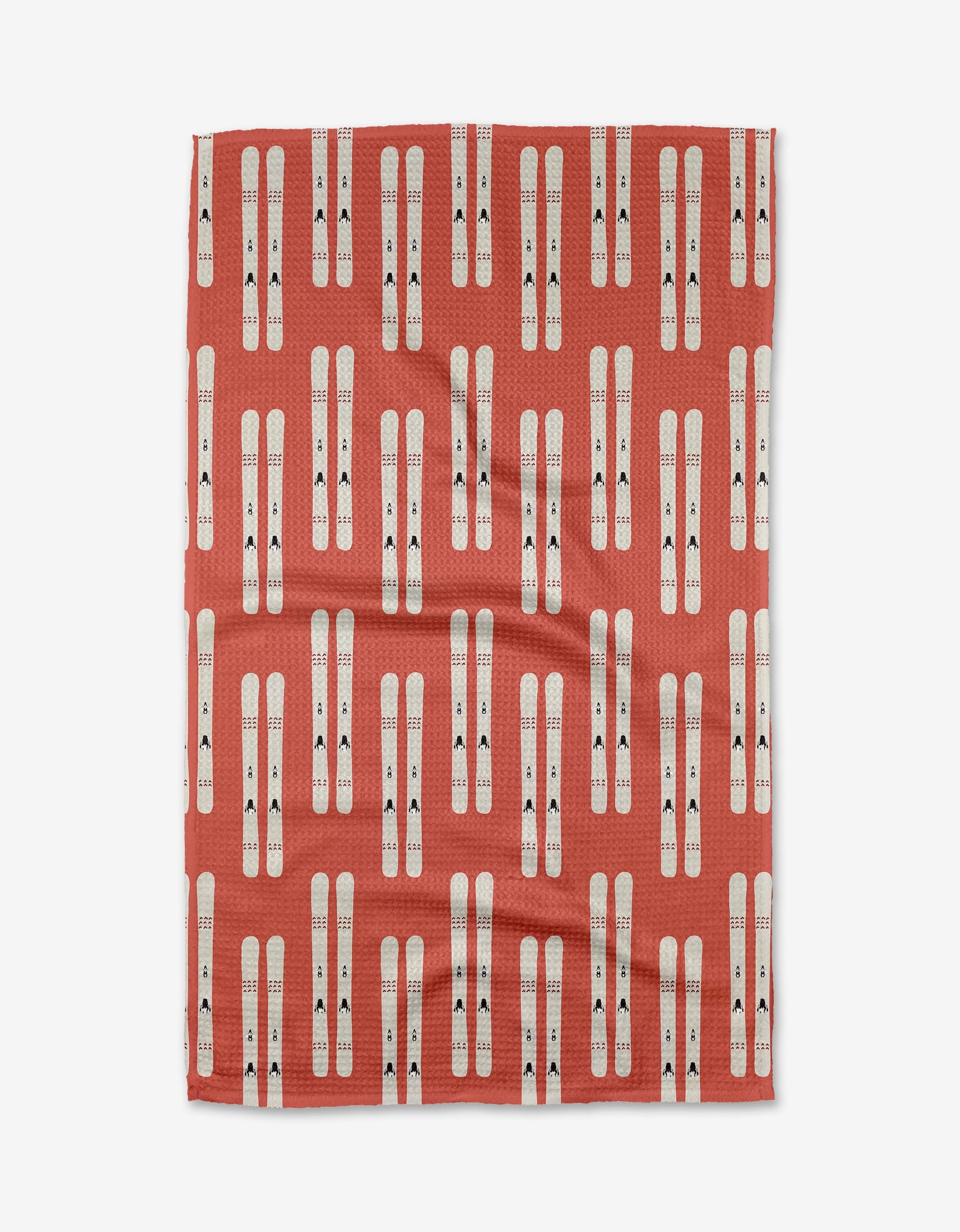 The Coit Creative Downhill Skis blanket is a quick-drying, reddish-orange throw, decorated with vertically arranged pairs of white skis featuring small black details in an even, repeating pattern.