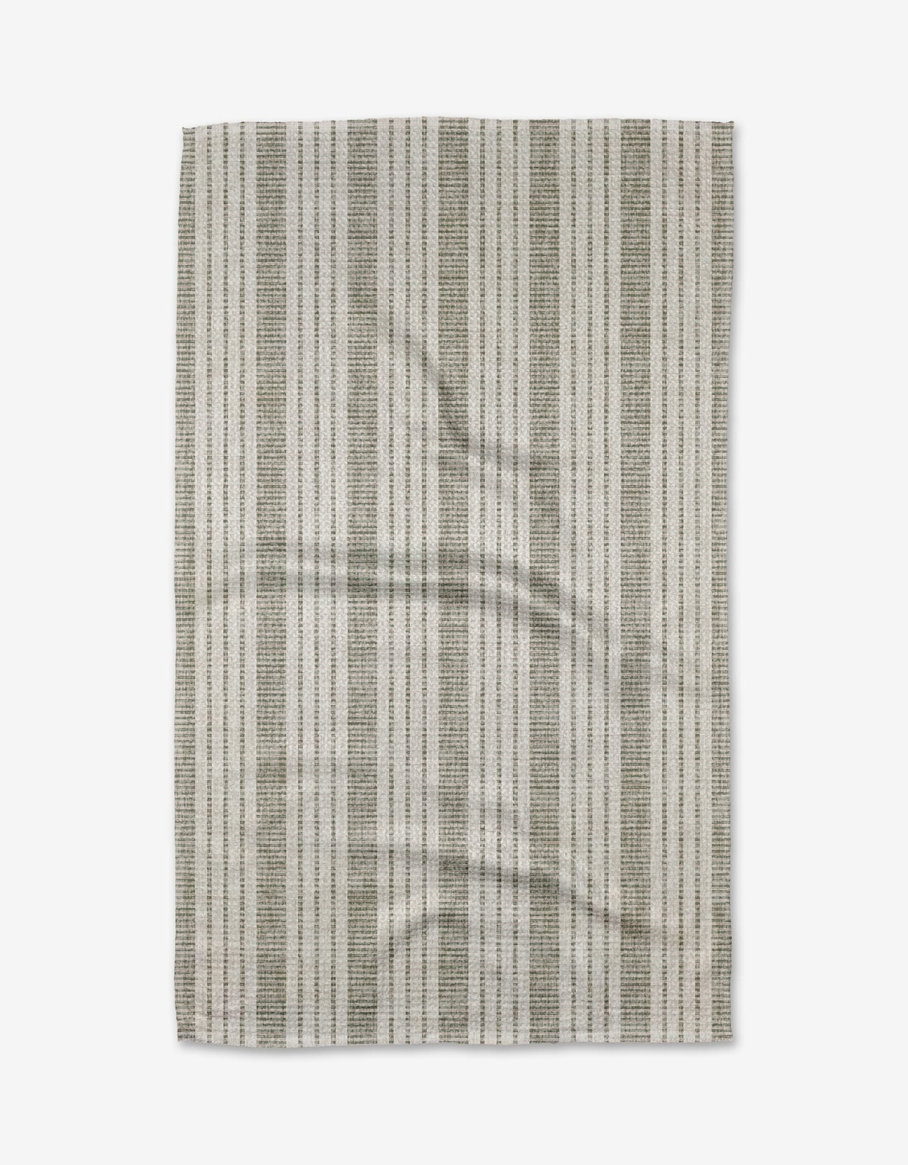 The Becki Owens Dyer Sage Tea Towel, made from ultra-absorbent Geoweave fabric, features a rectangular shape with vertical gray and white stripes, a subtle woven texture, and slight wrinkles, shown on a white background.