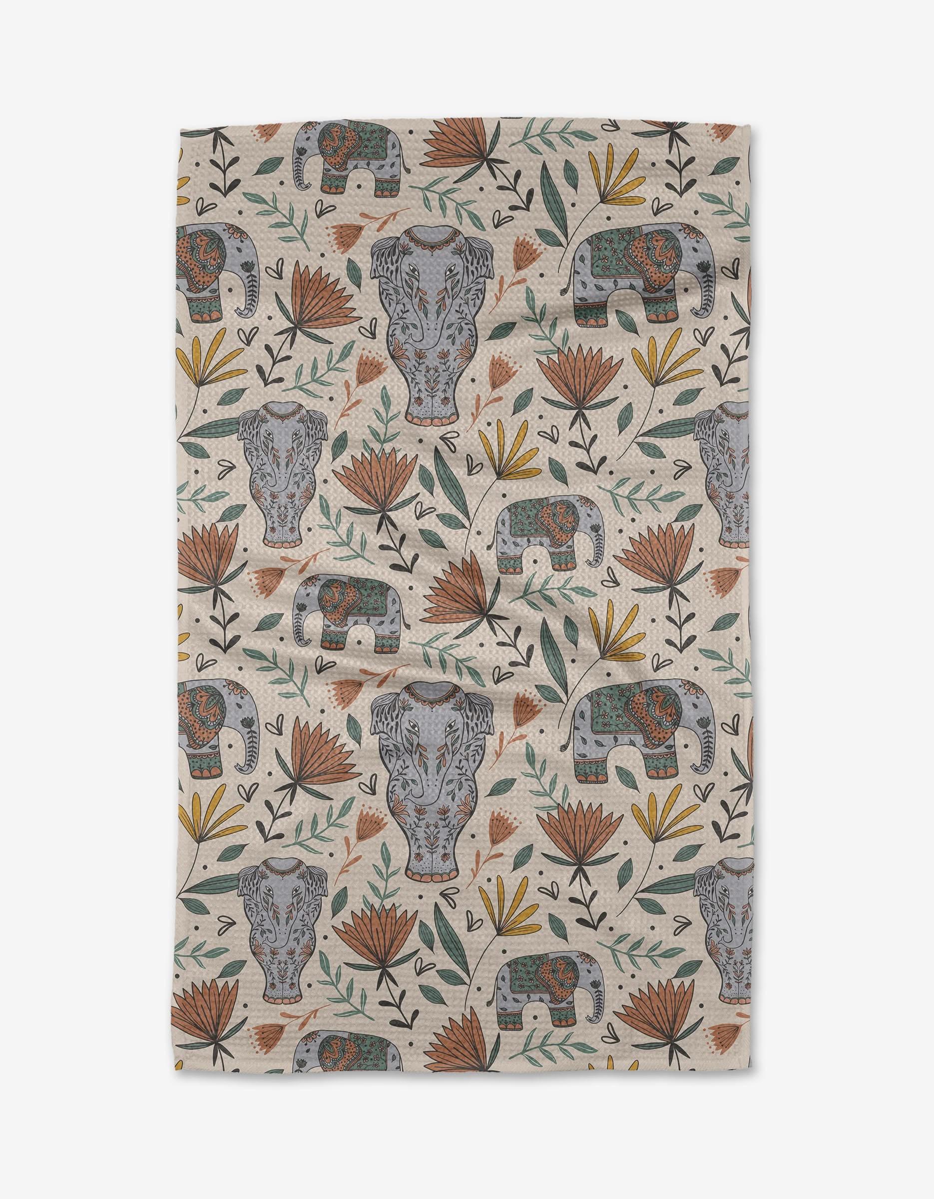 The Elephant Jungle tea towel by Amita Nair is beige, made from recycled materials, and features a symmetrical pattern of gray hippos, decorated elephants, orange-yellow flowers, and green leaves.