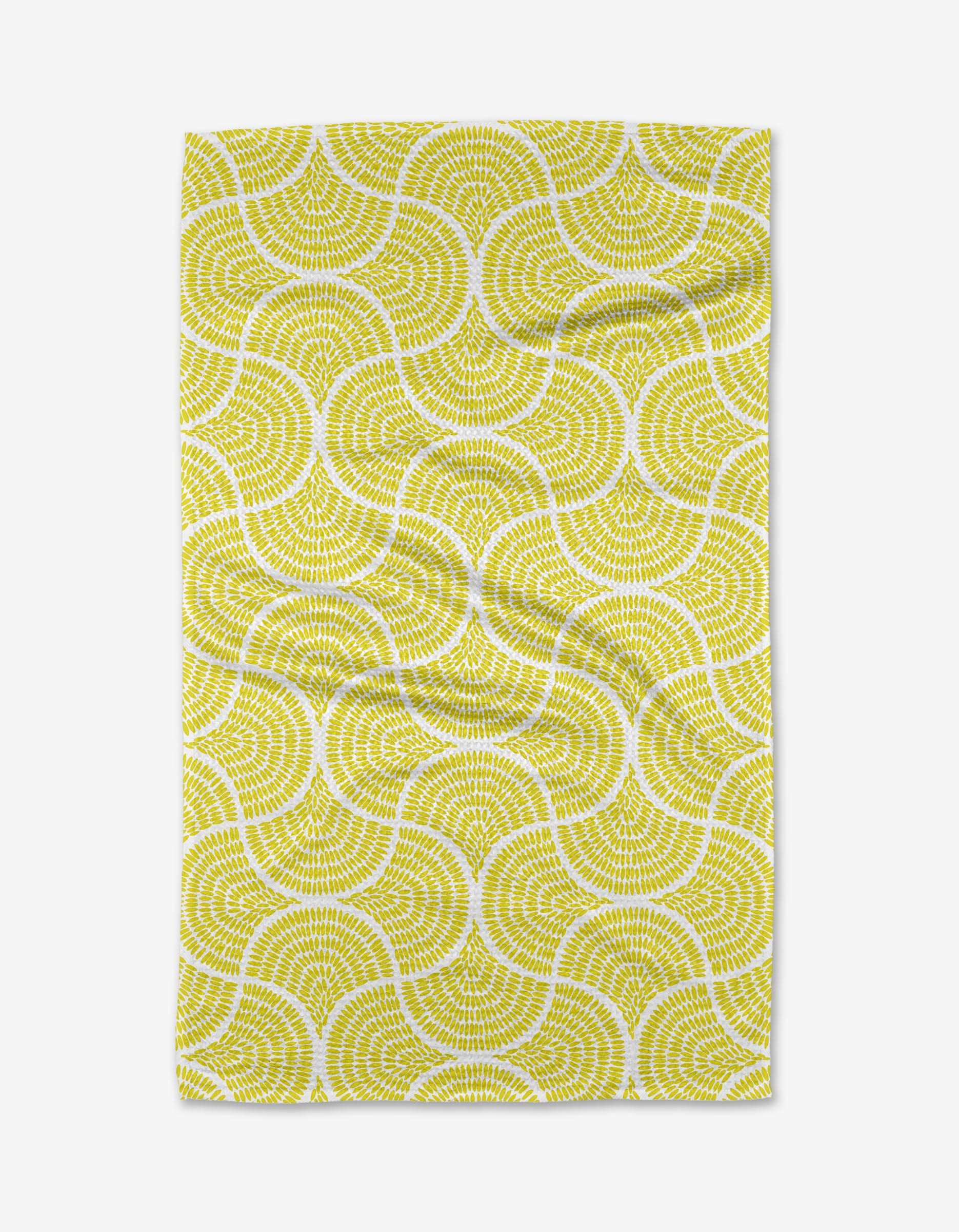 The Ferns tea towel by Dabney Lee features a repeating yellow and white wavy geometric pattern on a white background. Made from quick-drying recycled materials, the fabric has a slightly wrinkled appearance.