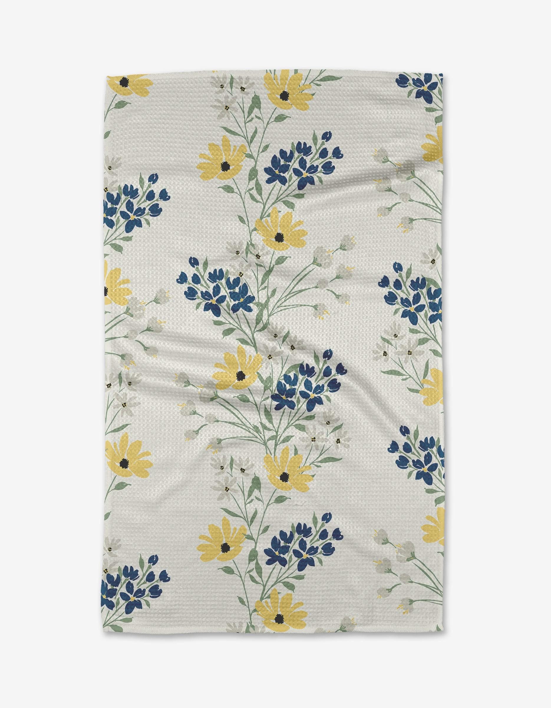 The Ashley Celena Garden Picks is a white textured blanket made from recycled materials, decorated with yellow, blue, and white floral patterns and green stems arranged diagonally on the fabric.