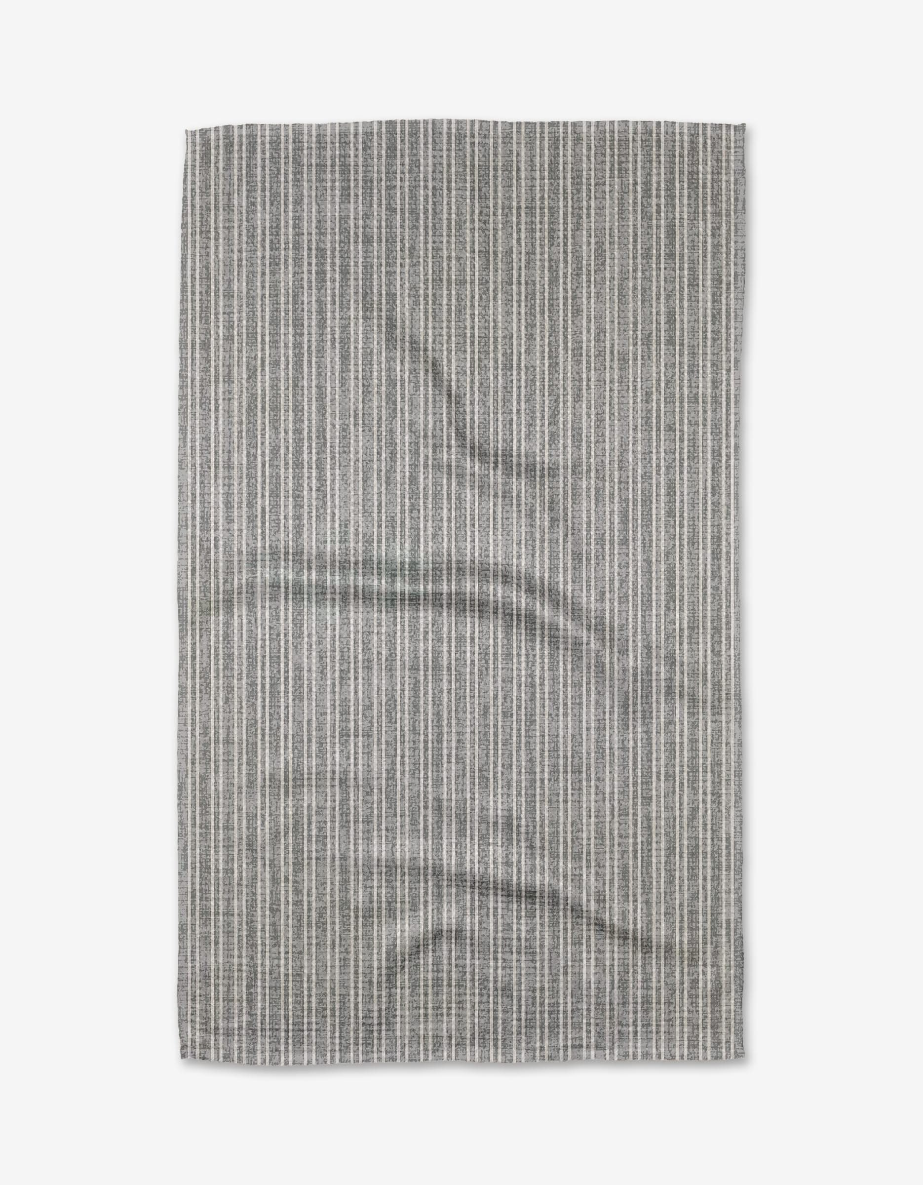 A rectangular Garff Grey tea towel by Becki Owens, featuring thin vertical white stripes and a slightly wrinkled texture, is laid flat on a white background.