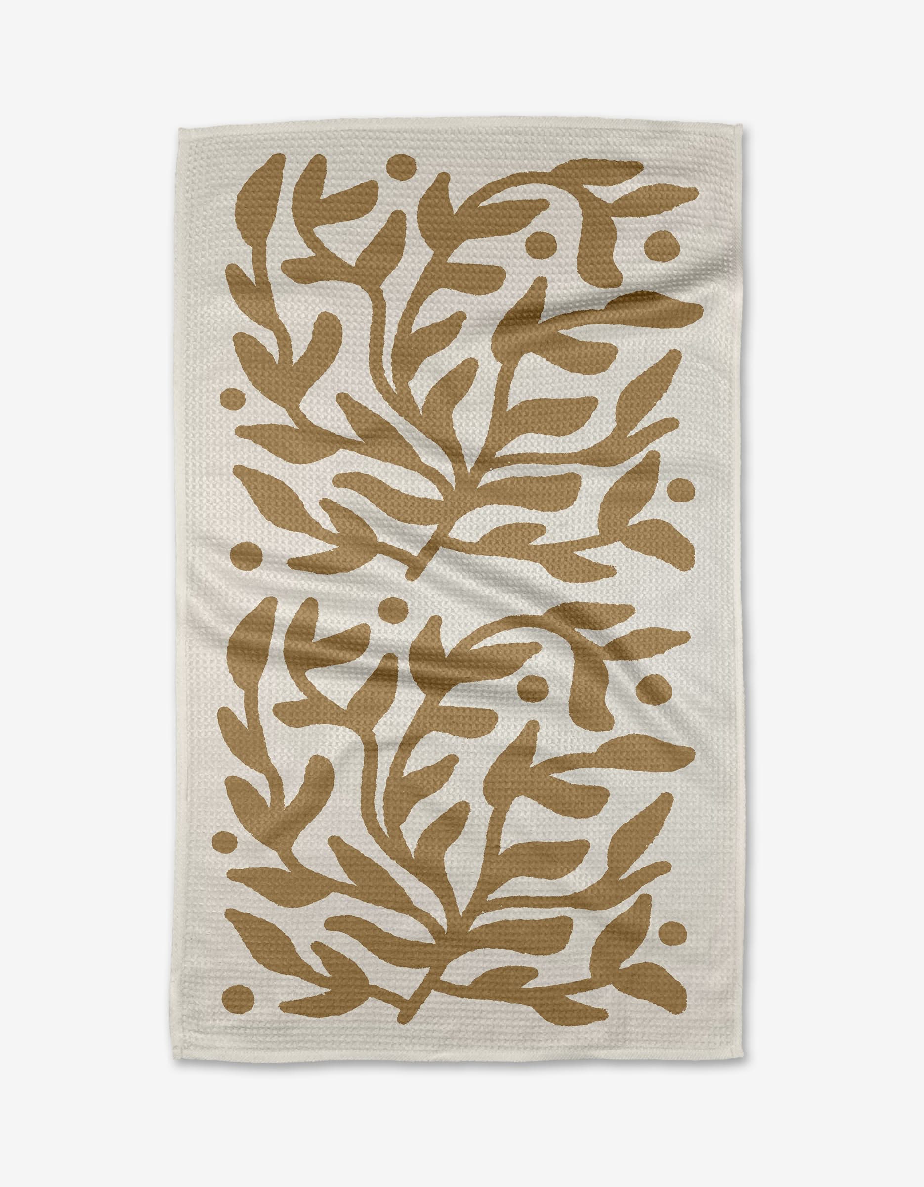 The Golden Garden tea towel by Graphics and Grain features a white, textured Geoweave fabric with symmetrical abstract brown leaves and dots in mirrored sections for durability and softness.